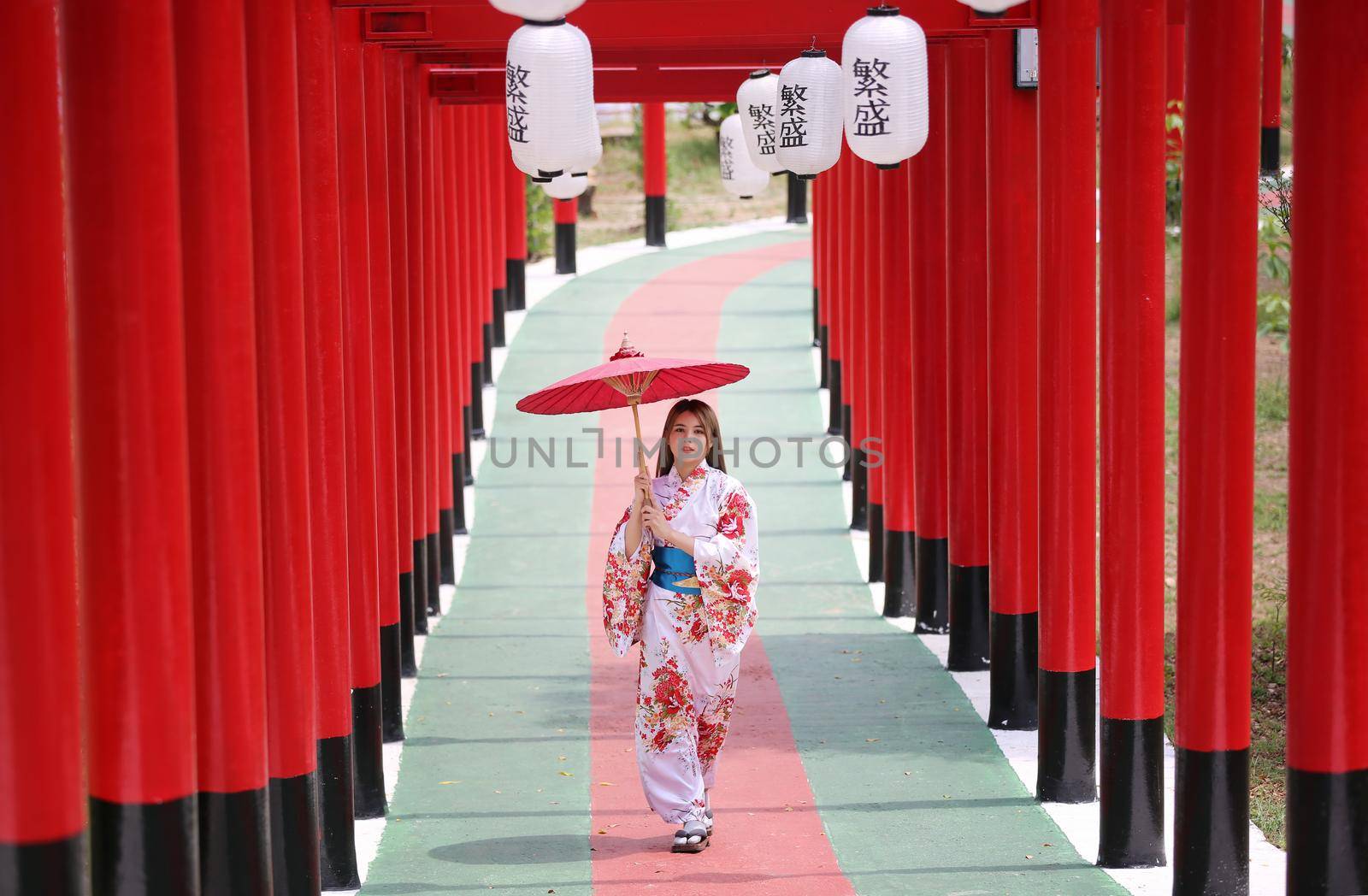 woman in kimono holding umbrella walking into at the shrine red gate, in Japanese garden.