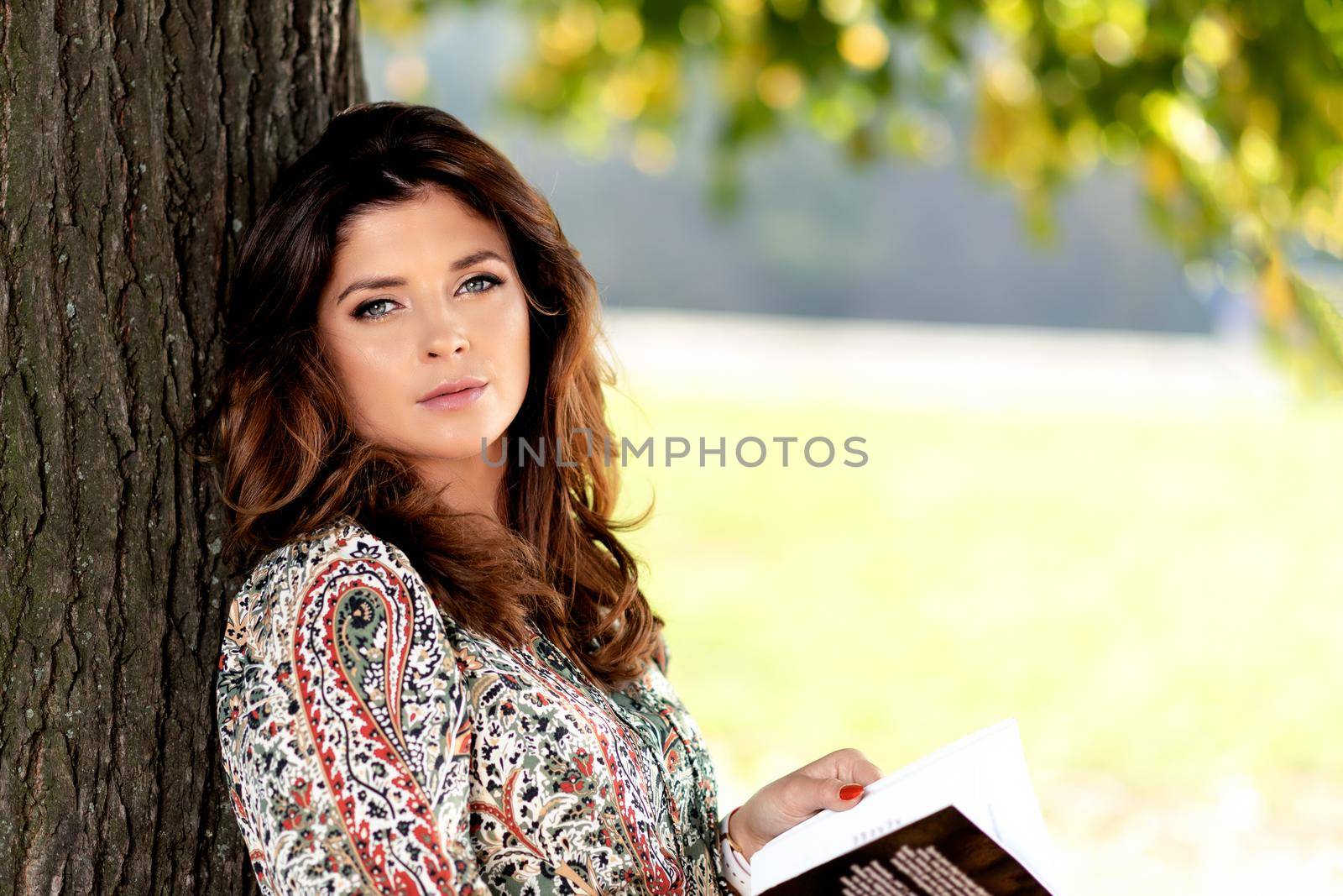 Portrait of a sensual and lovely woman with nice hairstyle reading book outdoor on a sunny day under the tree ( copy space)