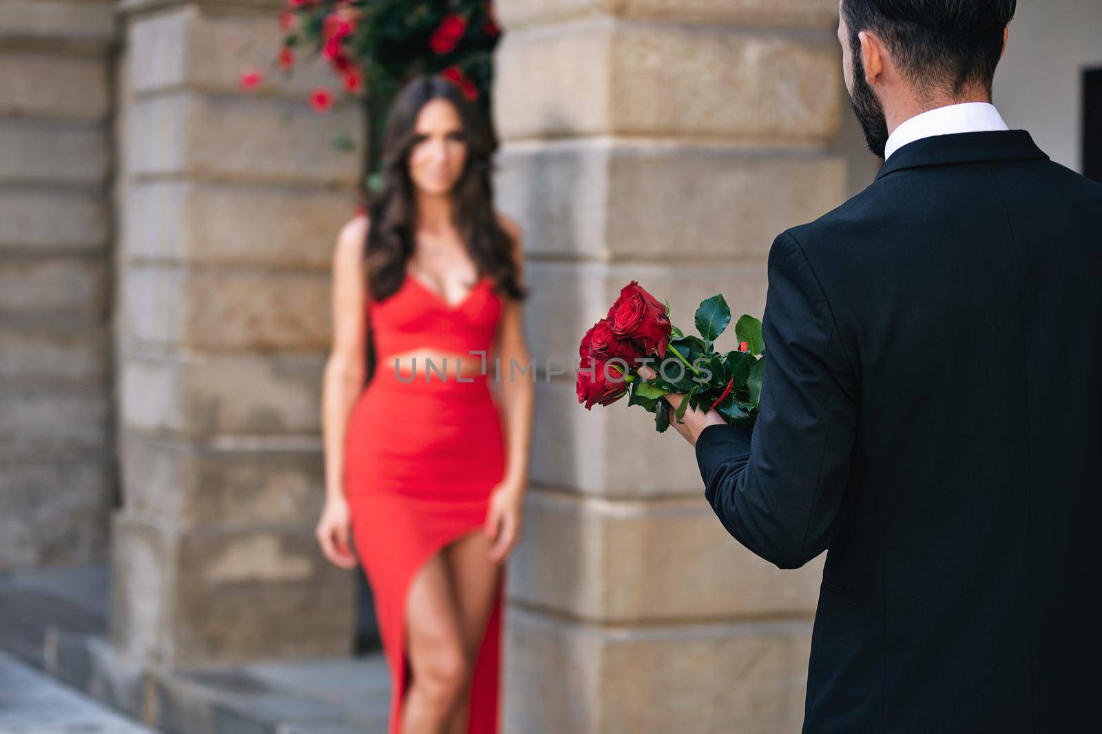 Back view of a man giving a bouquet of red roses to a woman during romantic dating.