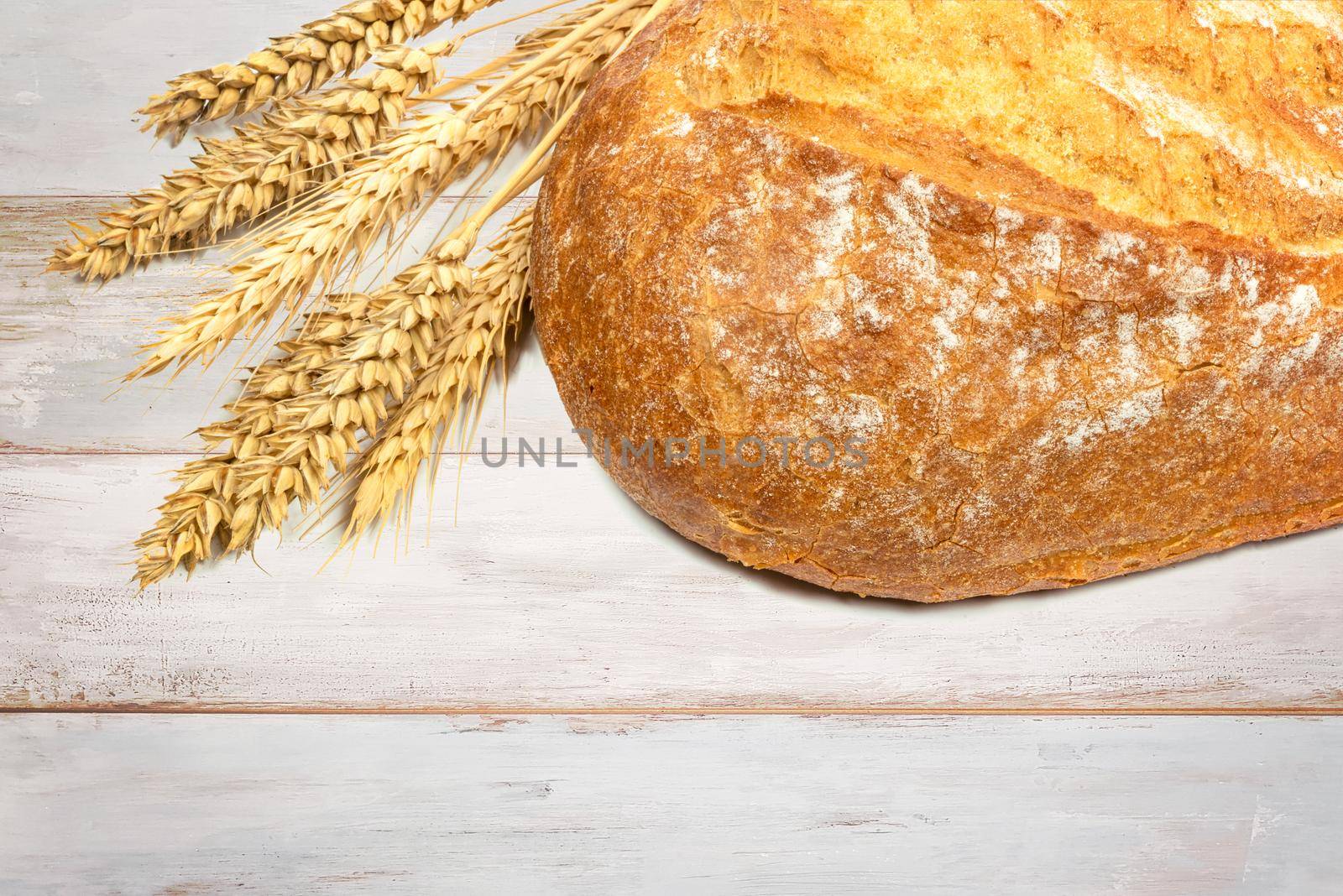 Fresh loaf of bread with wheat grains on a wooden vintage table in close up.