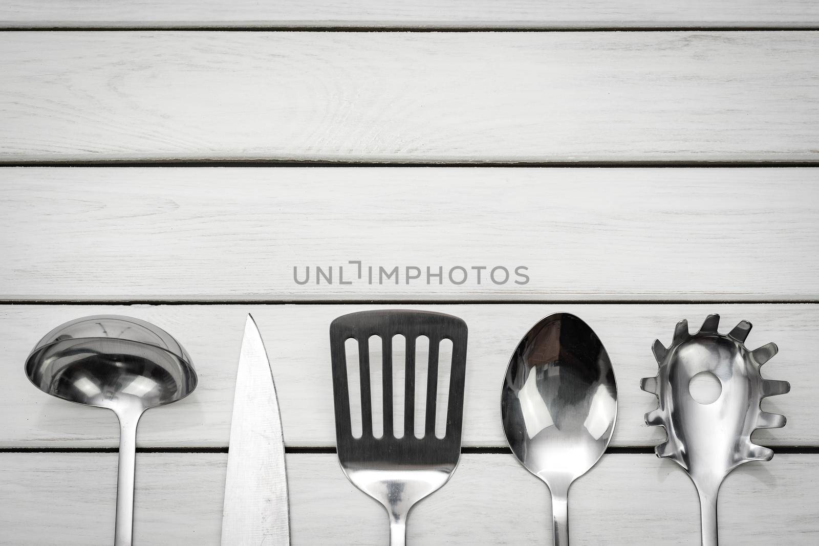 Top view of a silver kitchen utensil collection on a wooden table with copy space.