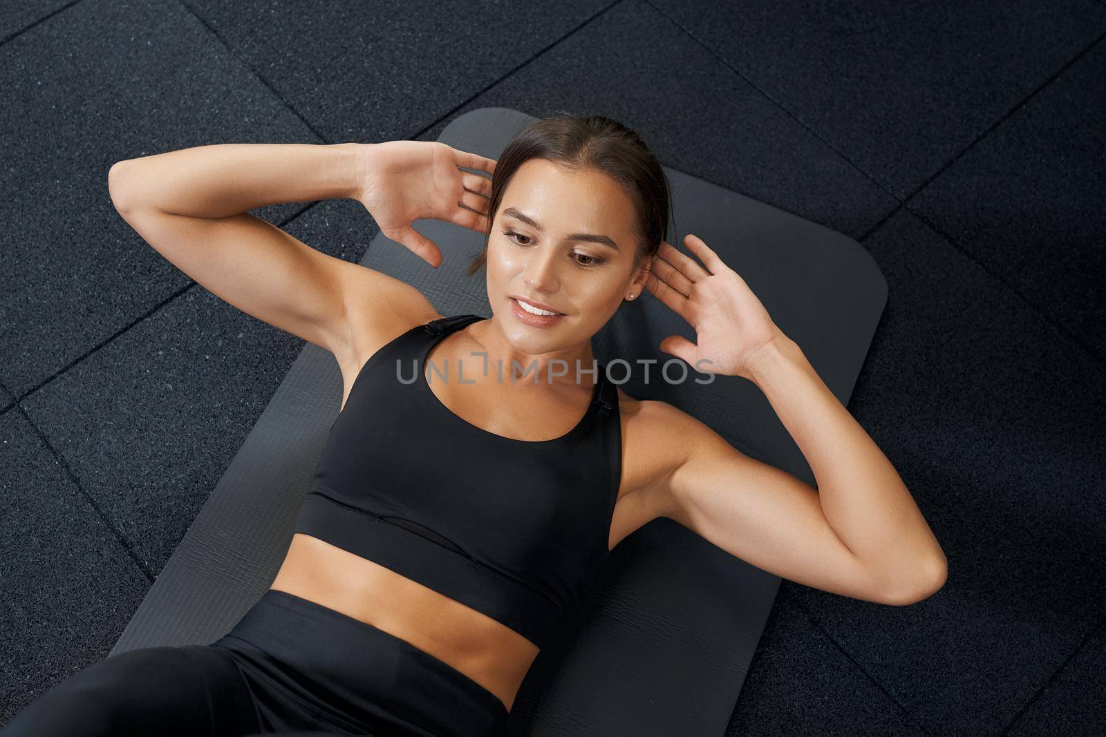 Brunette woman doing abs on black mat in gym. by SerhiiBobyk