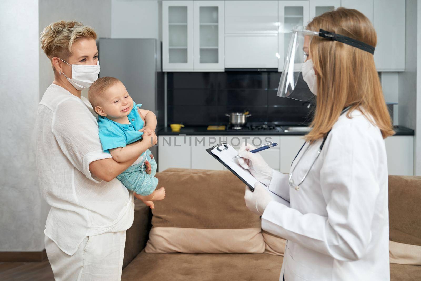 Qualified doctor in mask examining toddler at home by SerhiiBobyk