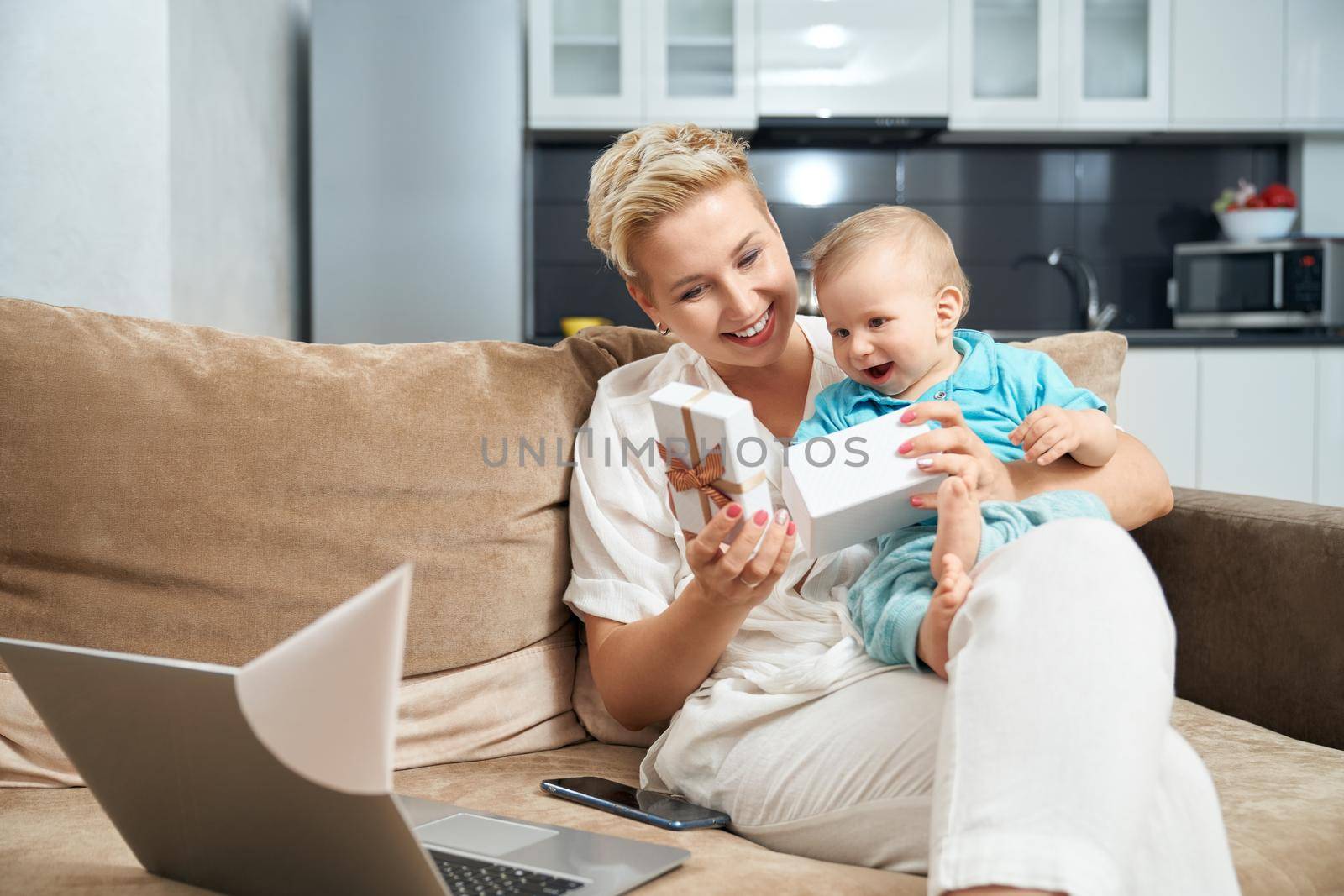 Woman with baby sitting on couch and opening present by SerhiiBobyk