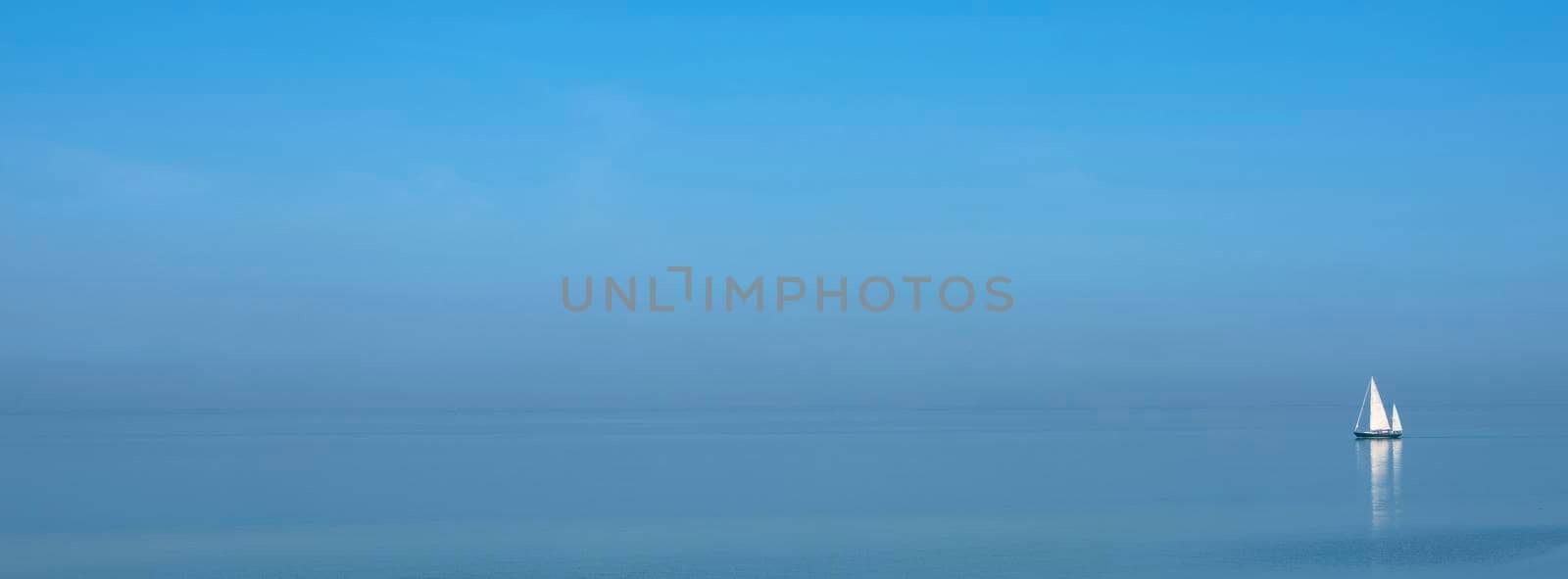 lonely sailing vessel on blue water of vast empty lake under blue sky by ahavelaar