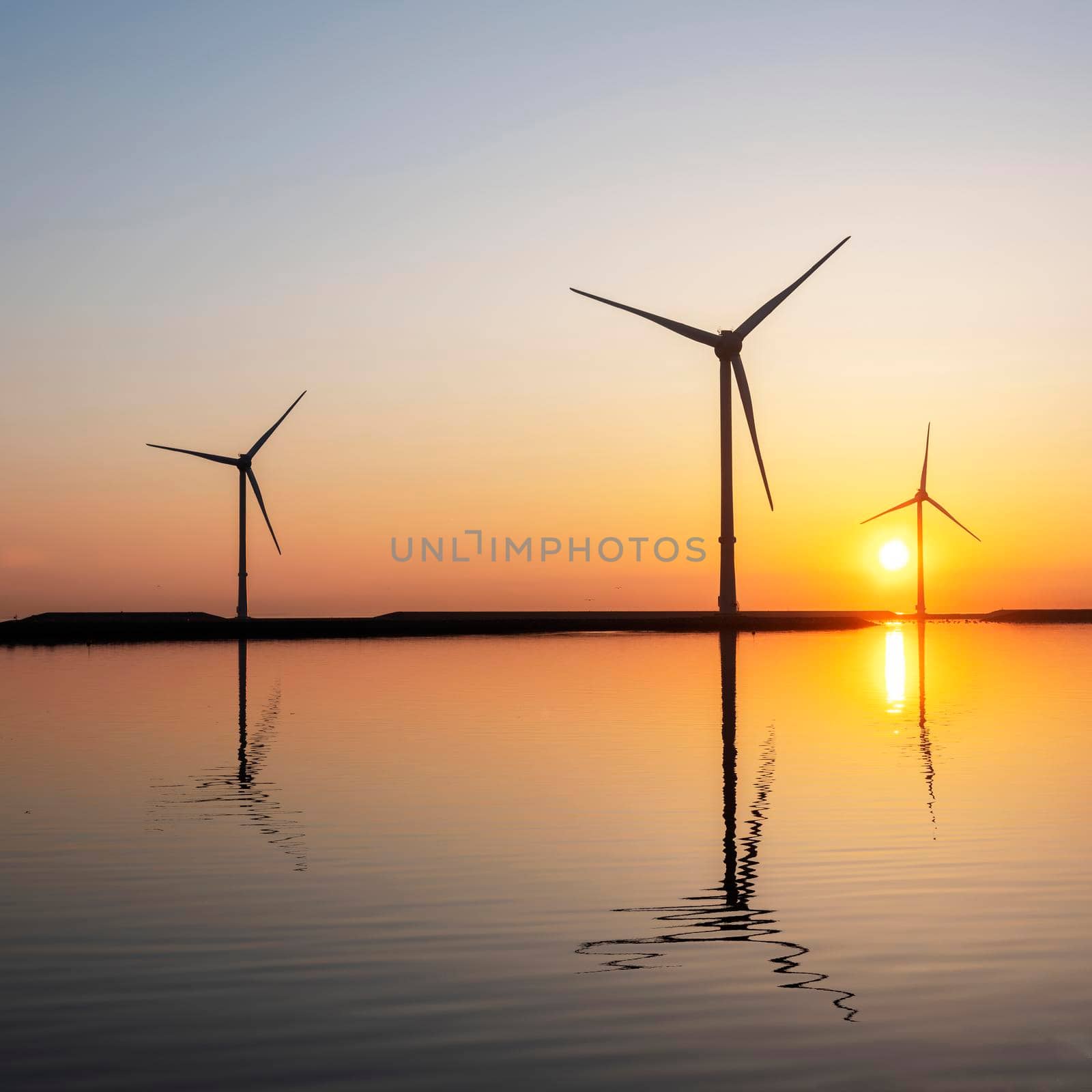 wind turbines and colorful sunrise reflected in water by ahavelaar