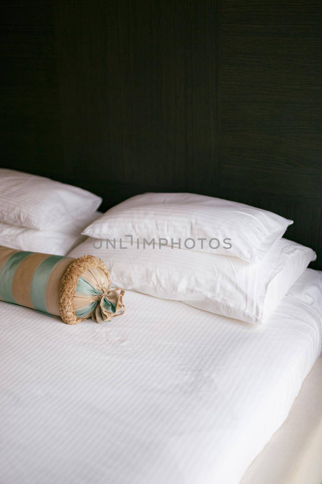 A bed with a white blanket and pillows of different sizes and an elongated cushion in a room with dark walls. High quality photo