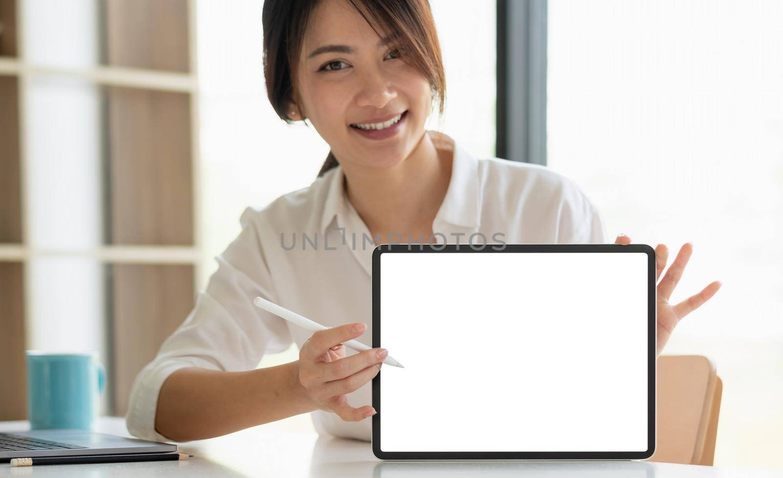 Smiling beautiful asian businesswoman showing blank tablet pc monitor, with copyspace area for slogan or text message. by nateemee