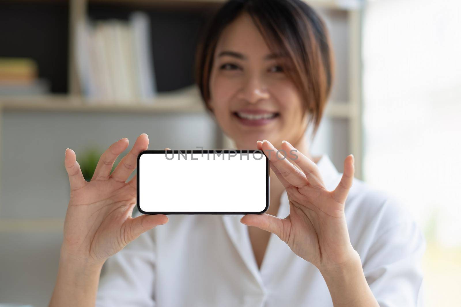 Smiling beautiful asian businesswoman showing blank smartphone monitor, with copyspace area for slogan or text message. by nateemee