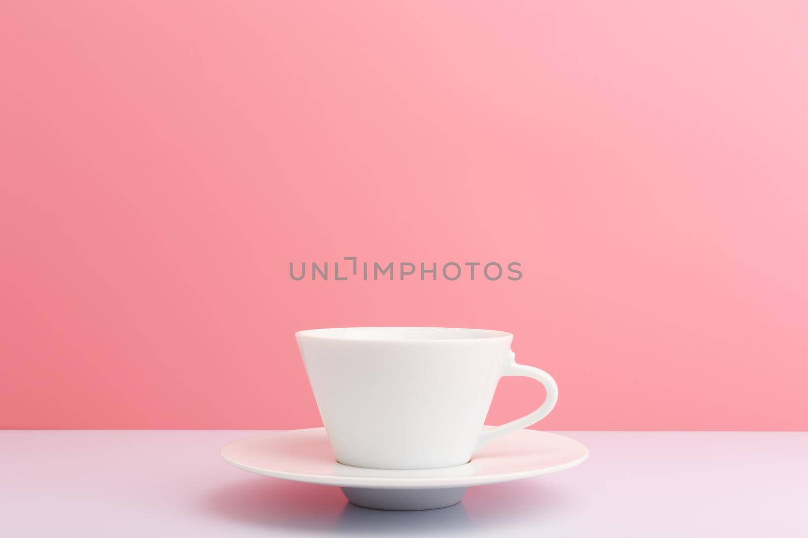 White ceramic coffee cup with saucer on white table against light pink background with copy space. Concept of hot drinks and kitchen utensil