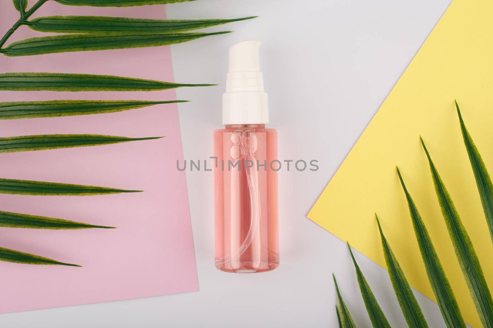 Face cleaning foam in transparent tube with dispenser on white table with yellow and pink paper and palm leaves by Senorina_Irina