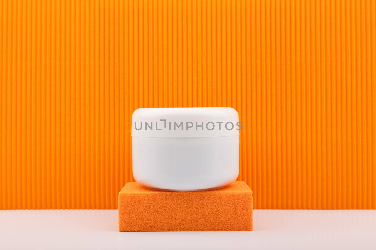 White cosmetic jar on orange podium against orange background. Concept of beauty products with citrus extracts. Cosmetic jar with cream, mask or scrub against colored background with copy space