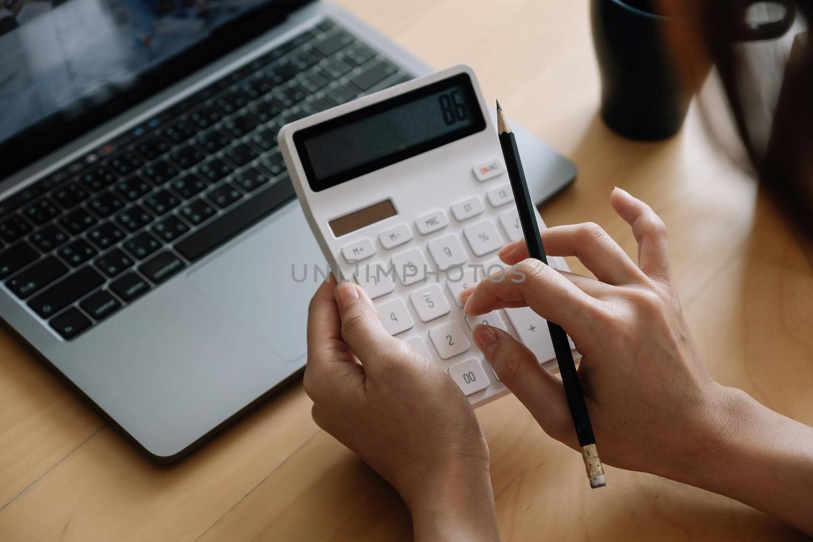Close up of businesswoman or accountant hand holding pencil working on calculator to calculate financial data report, accountancy document and laptop computer at office, business concept
