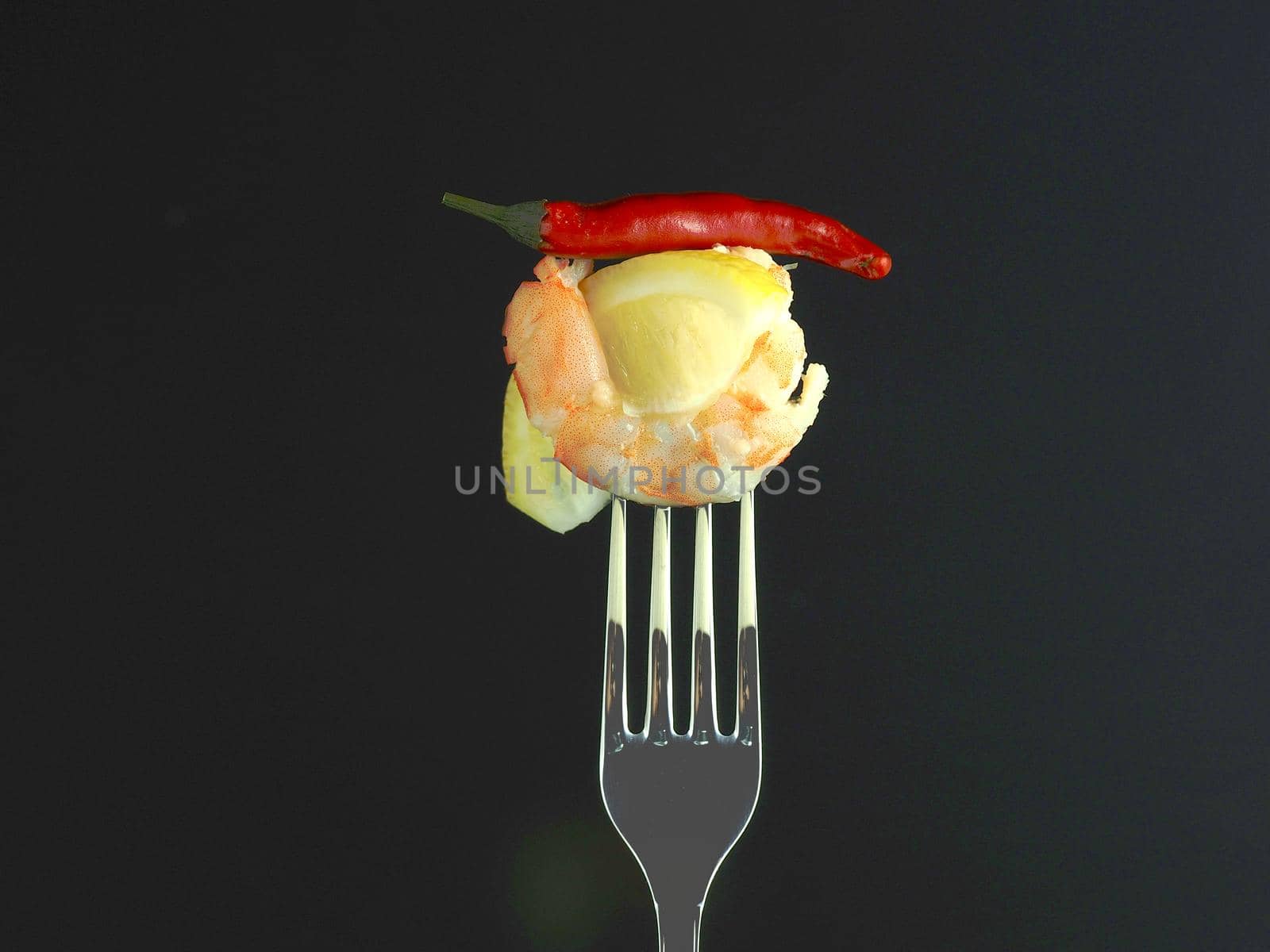 Shrimp on a fork. Prawn meat boiled on a fork with lemon t red pepper on a black background. High quality photo