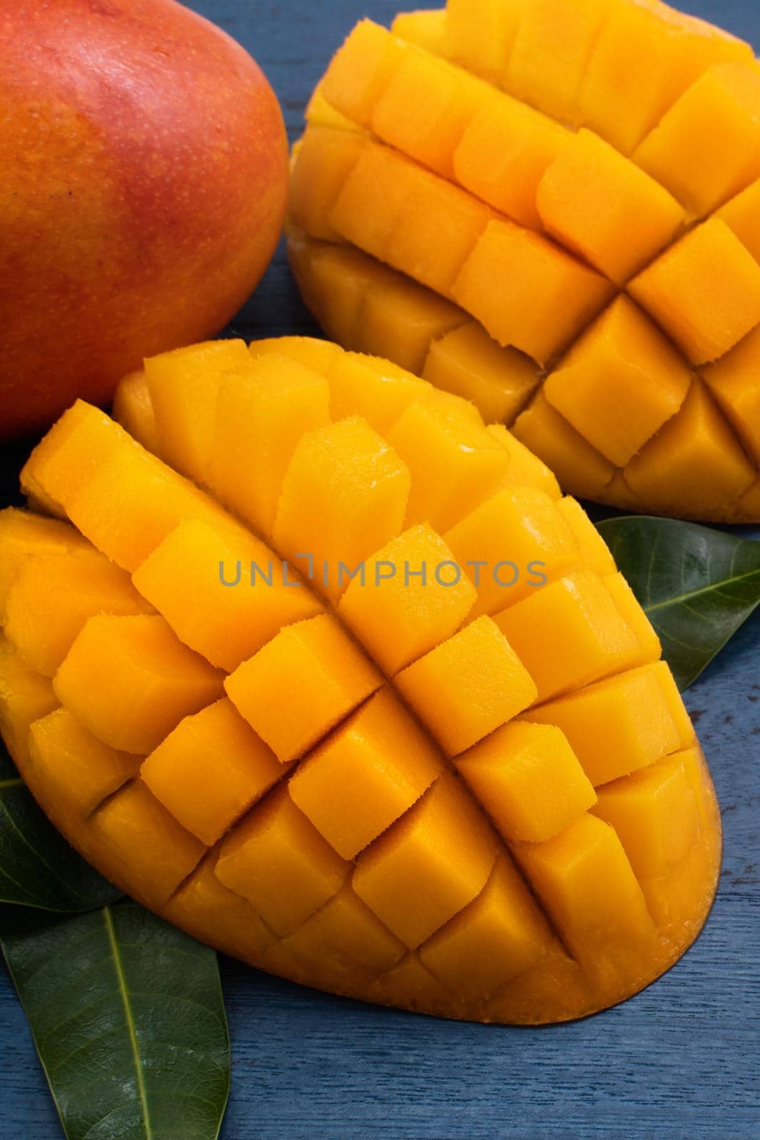 Top view design concept of beautiful mango tropical fruit with sliced chuncks over blue table background.