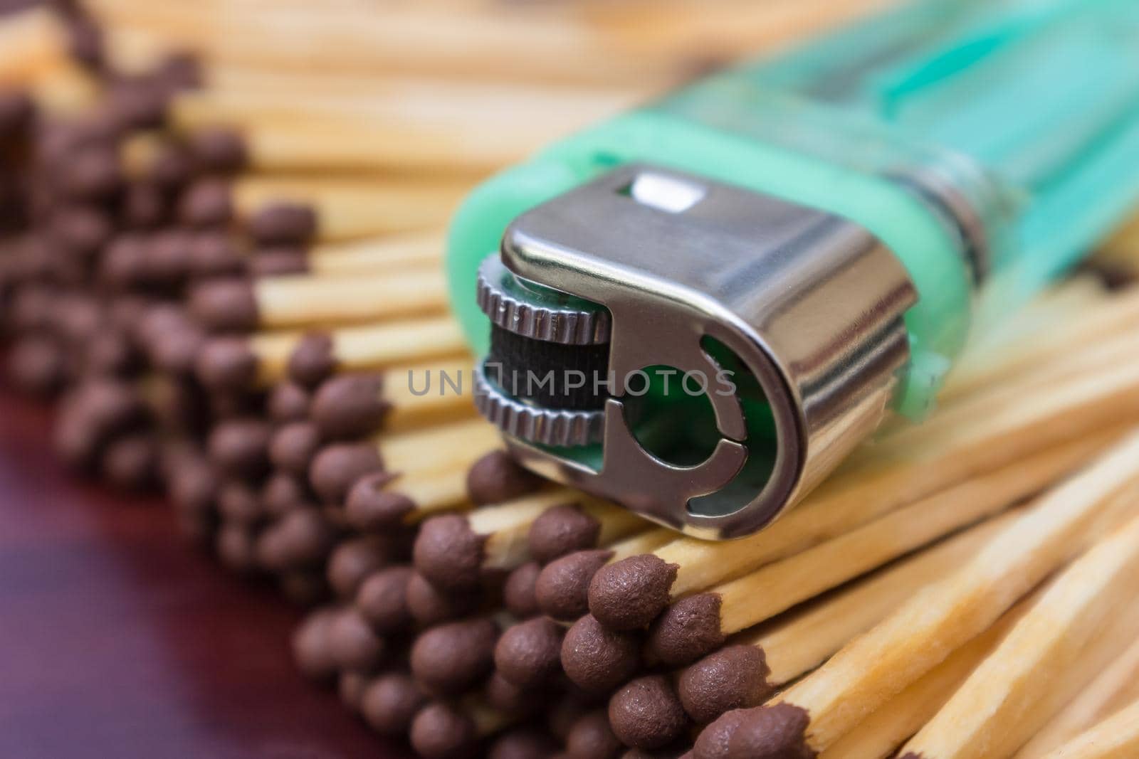 A green pocket lighter lies on a pile of wooden matches close-up