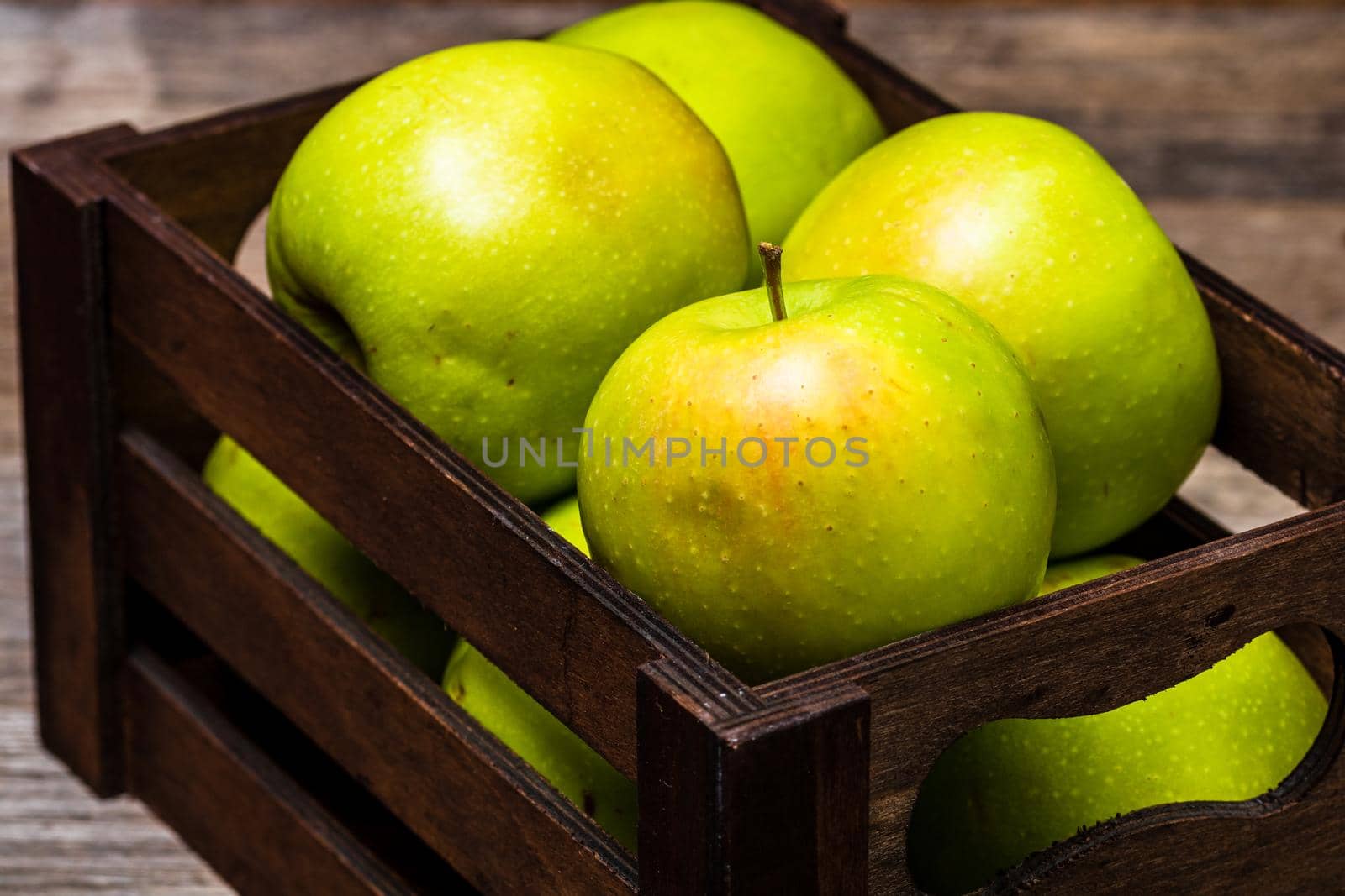 Wooden crate with ripe green apples on wooden table.