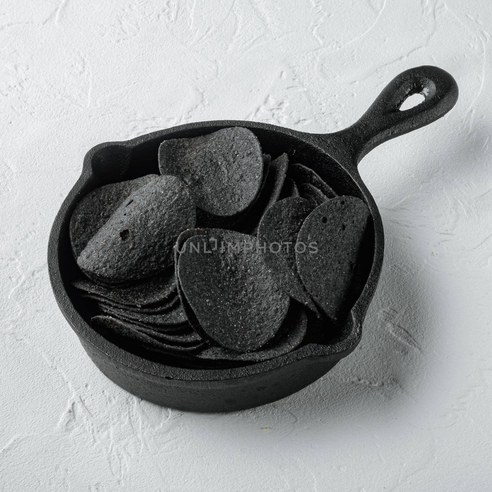 Black crispy potato chips, in cast iron frying pan, on white stone surface, square format by Ilianesolenyi