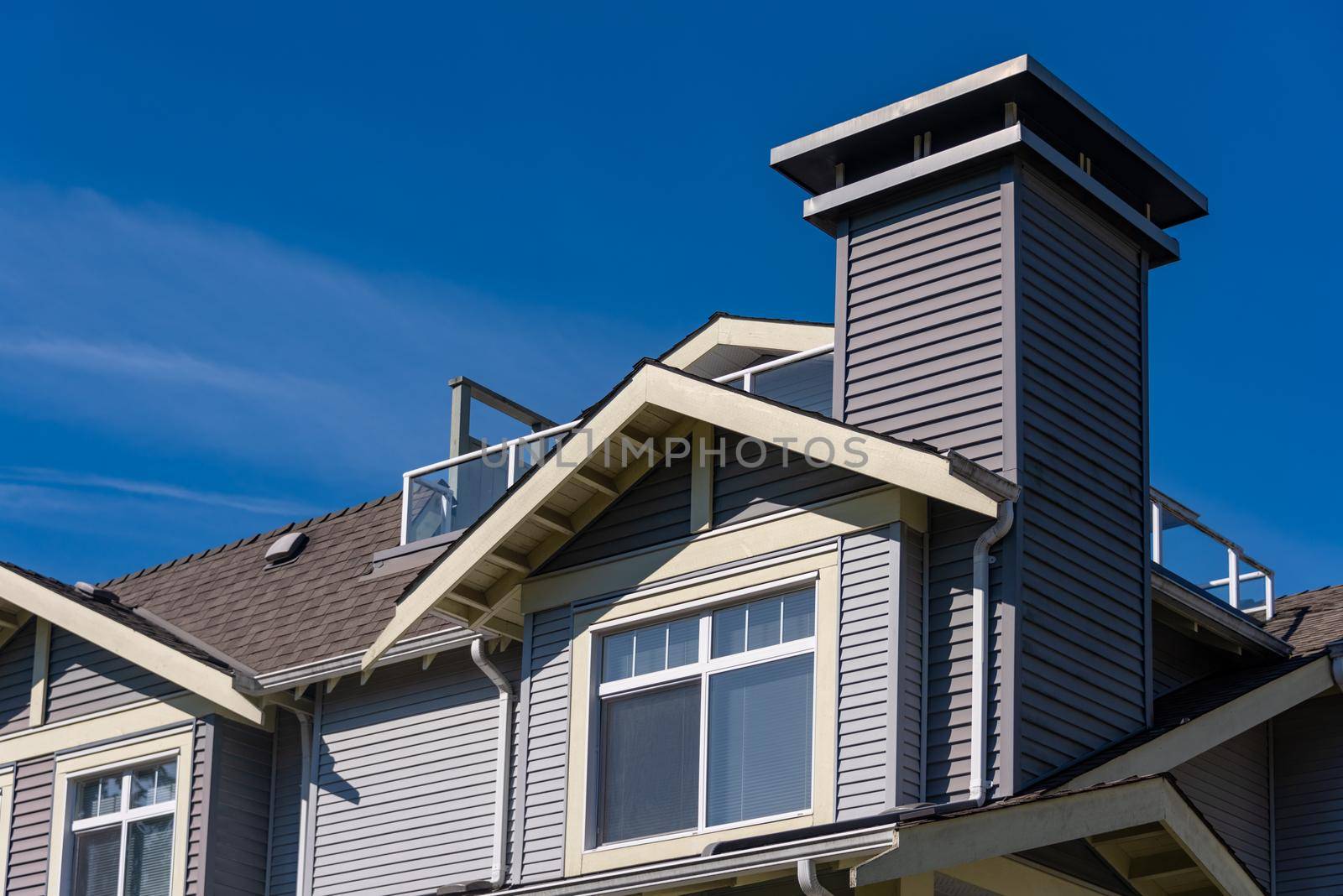 Window on upper level of residential building. Low rise building with patio on the roof on blue sky background
