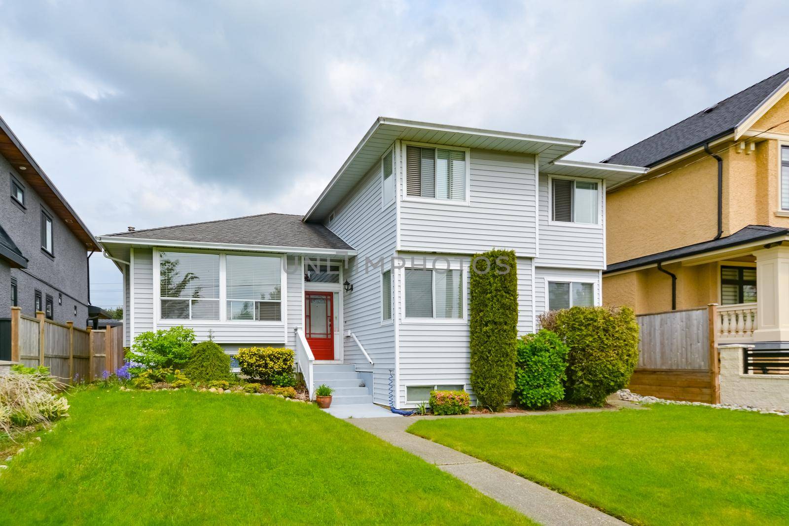 Main entrance of residential house with concrete pathway over green lawn on the front yard on cloudy day