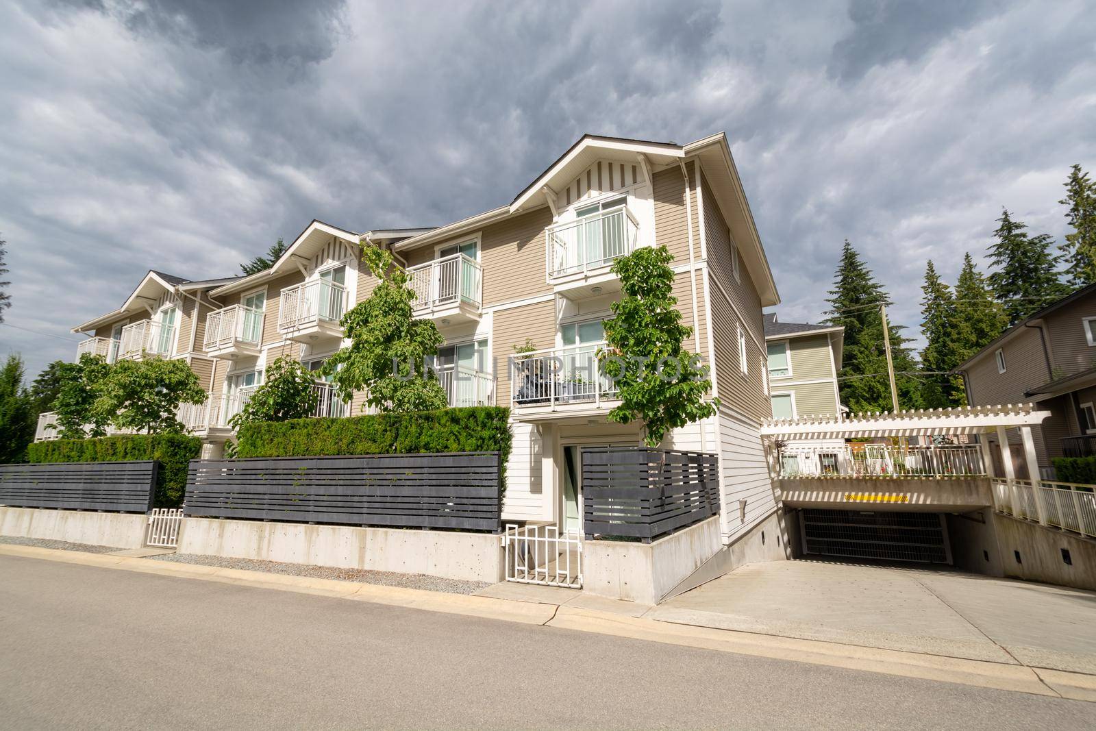 Residential apartment building with concrete driveway to underground garage. Residential condo building with fenced front yard on stormy sky background