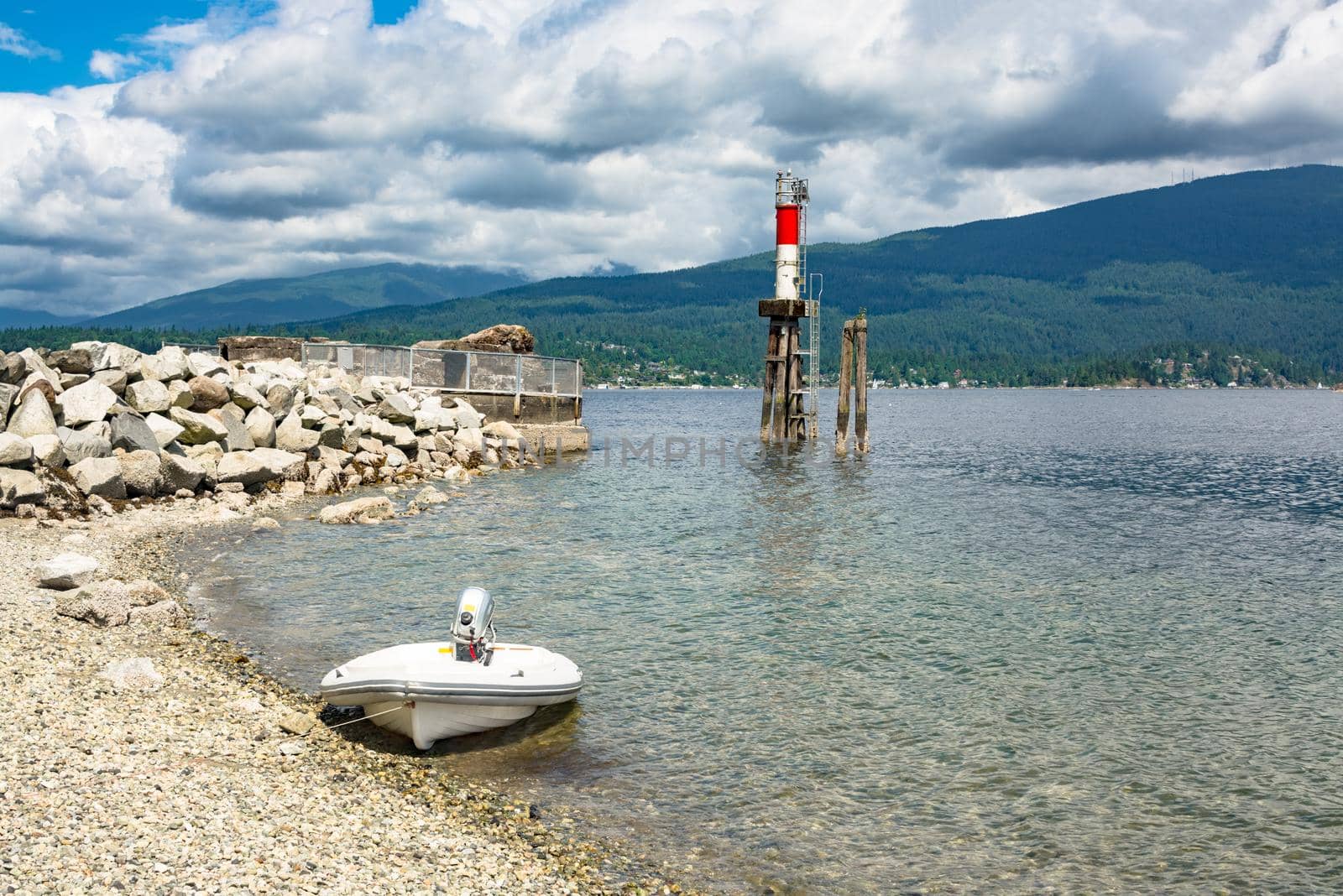 Motorized boat moored at stone shore with ship channel light behind