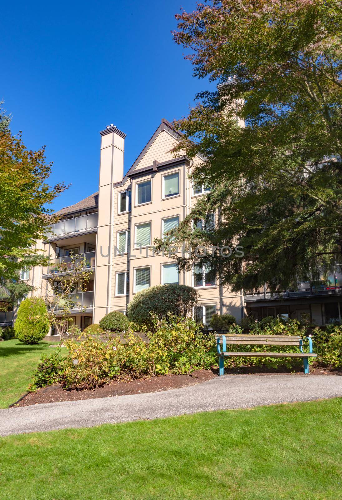 Low rise residential building and wooden bench in front. Apartment building and small park area on sunny day