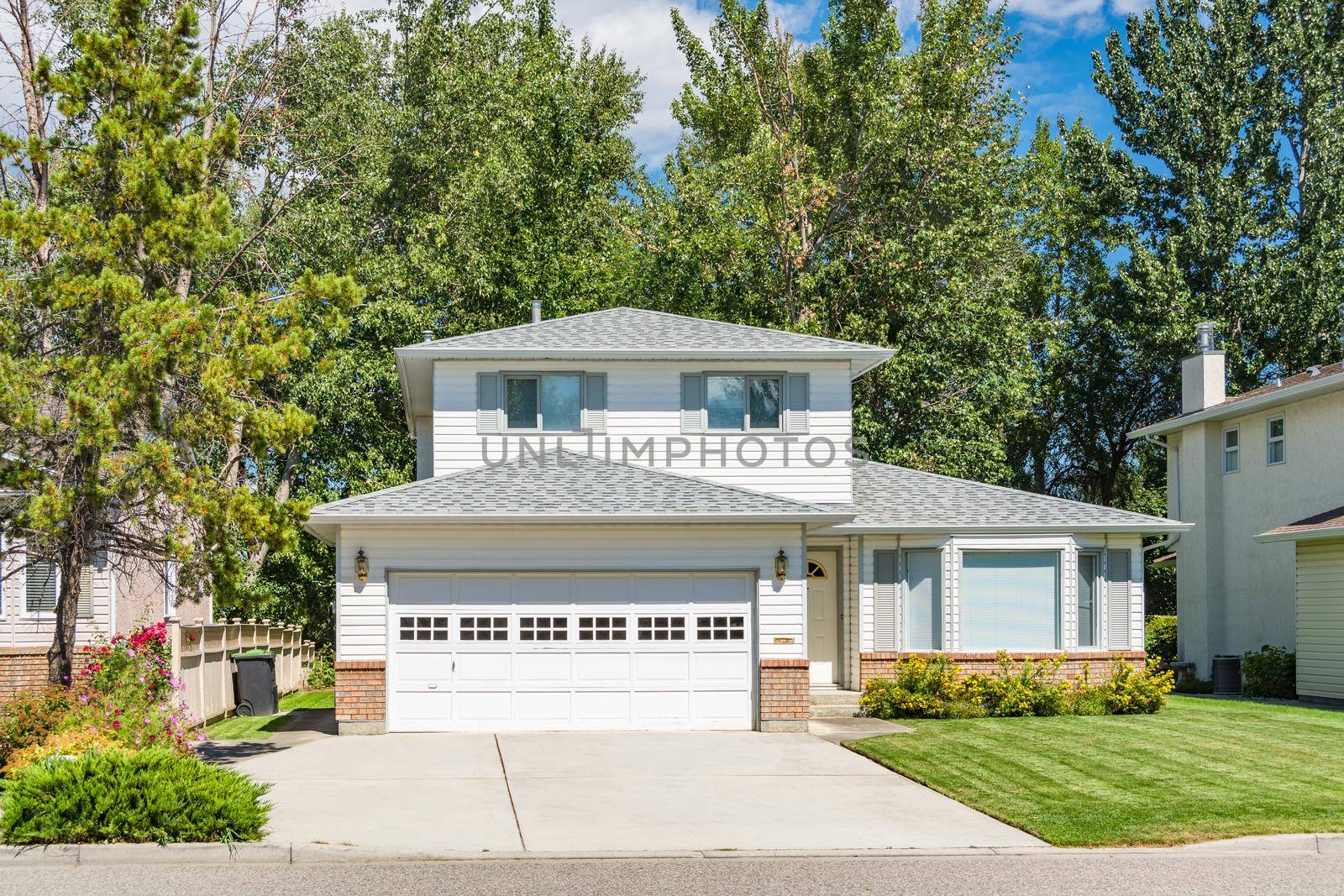 A perfect neighbourhood. Family house with landscaped front yard and concrete driveway. Residential house with wide garage on sunny day in British Columbia