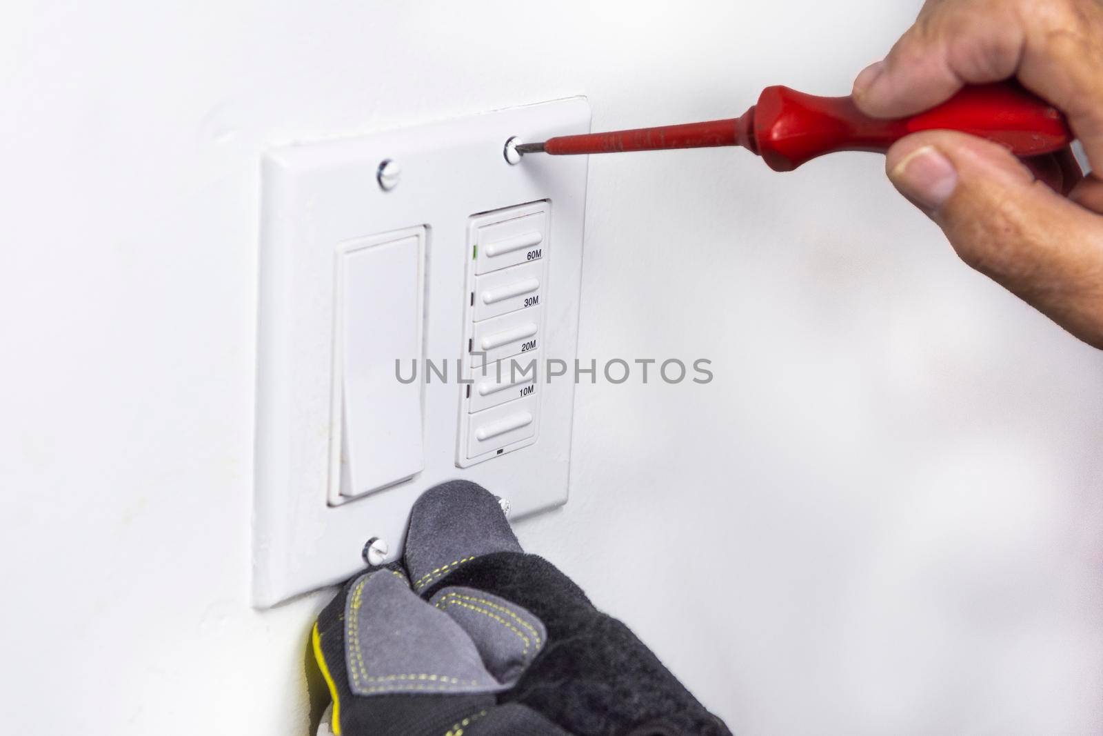 The electrician prepared the screws for securing the switch cover and inserted them into the holes, holding them in place with a screwdriver.