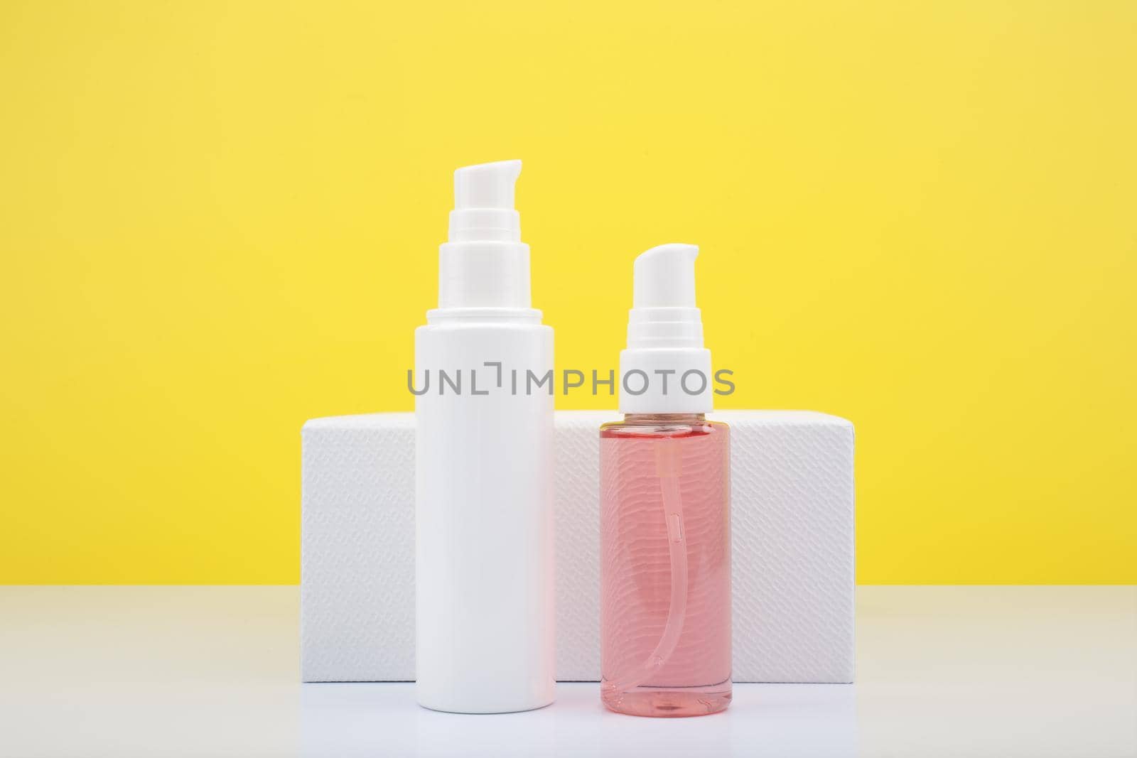 Face cream in white tube and pink cleansing foam in transparent tube against yellow background with copy space. by Senorina_Irina