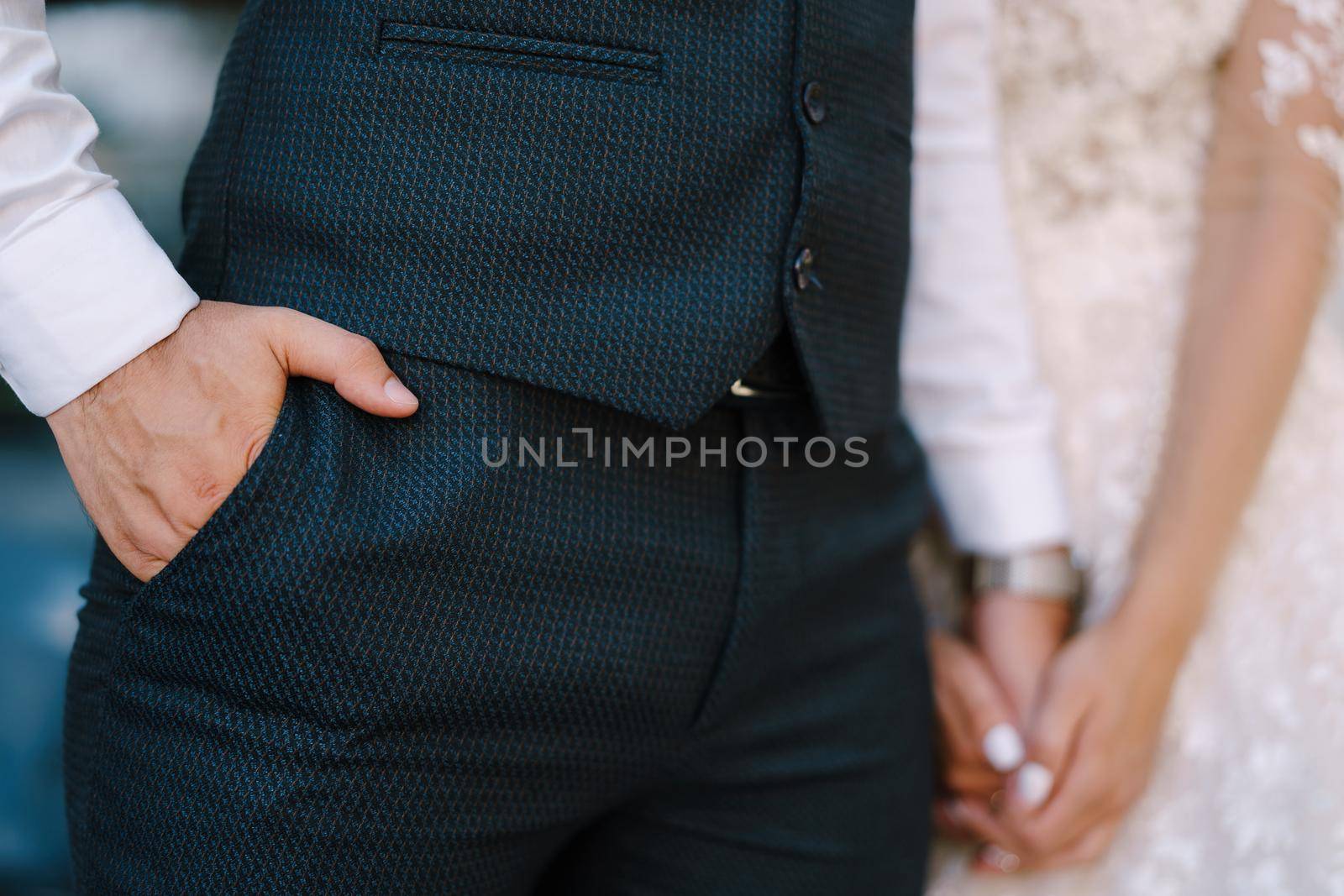 Groom in a navy suit holding his hand in his pocket. Bride is holding his other hand with hers. Fine-art wedding photo in Montenegro, Perast. by Nadtochiy