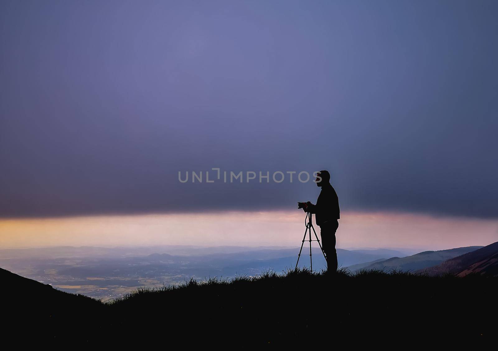 Silhouette of photographer with camera on tripod at cloudy sunset in Karkonosze Giant Mountains