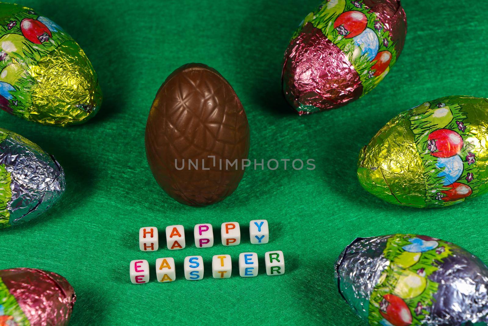Happy Easter text with chocolate egg and colorful foil wrapped eggs on green
