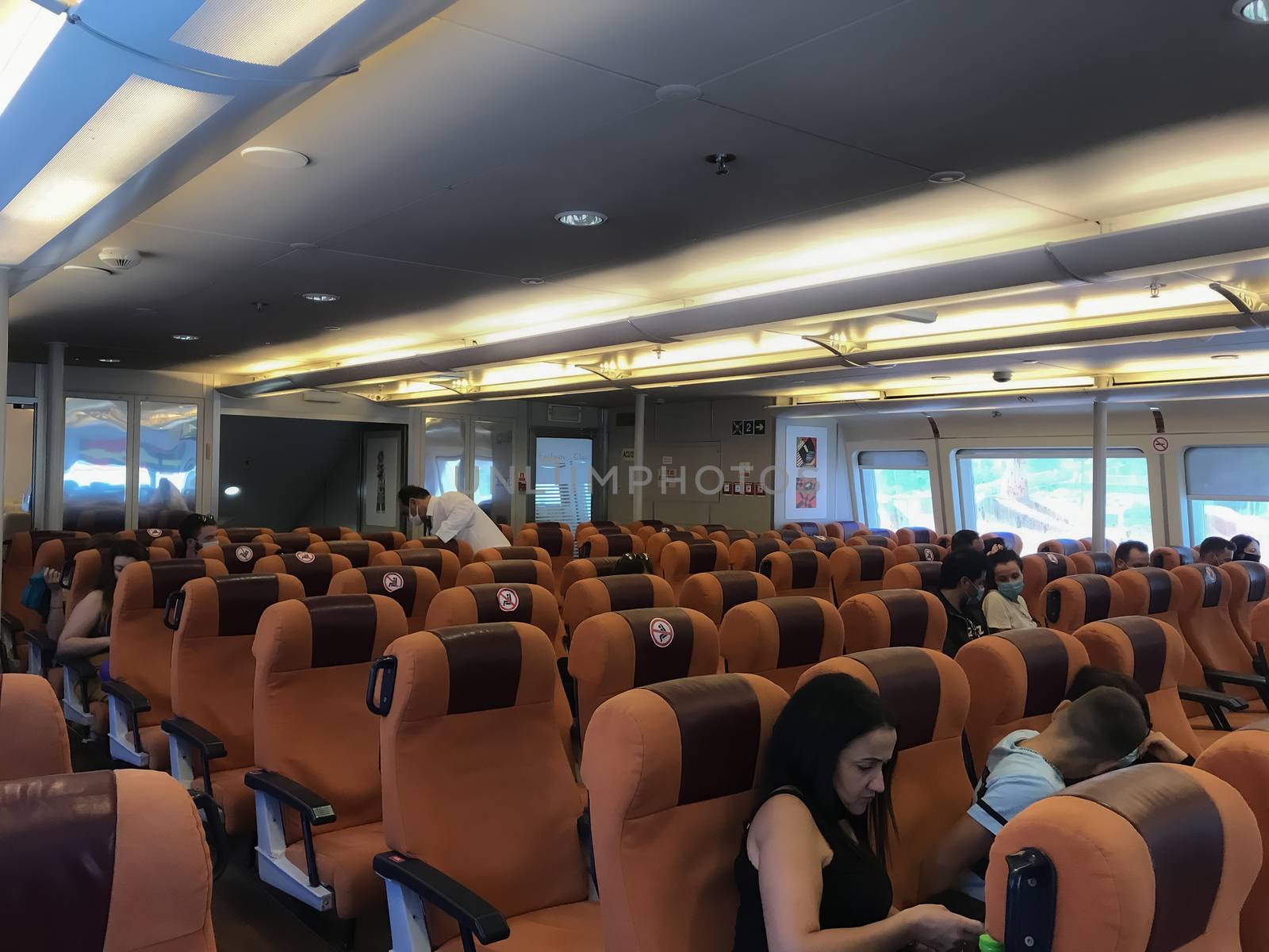 People with face protection at boat with keep empty seats distance designation embarking from a Hellenic seaport.