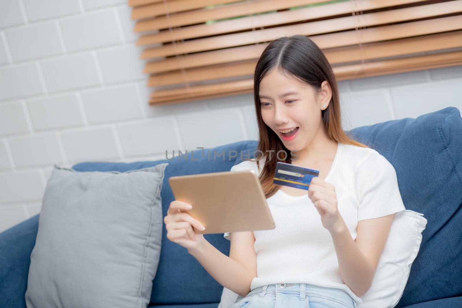 Young asian woman smiling holding credit card shopping online with tablet computer buying and payment, girl using debit card purchase or transaction of finance, lifestyle and e-commerce concept.