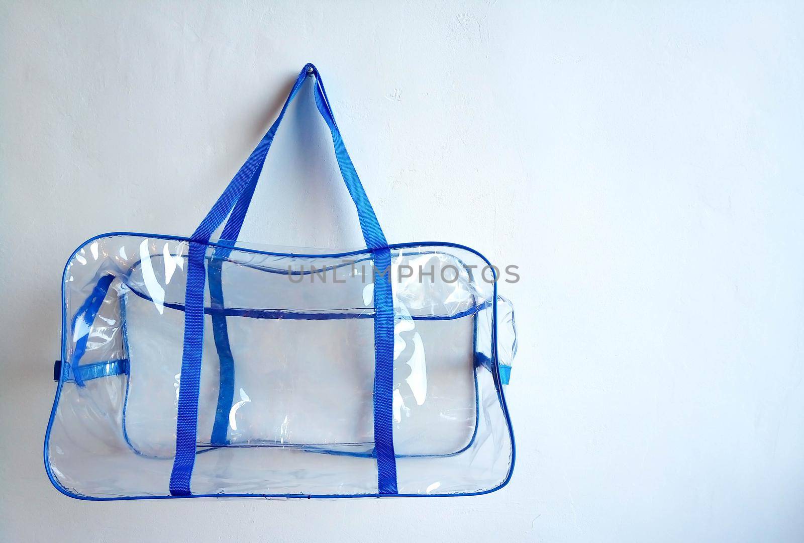 Plastic bag with blue handles hanging on a nail, on a white background.