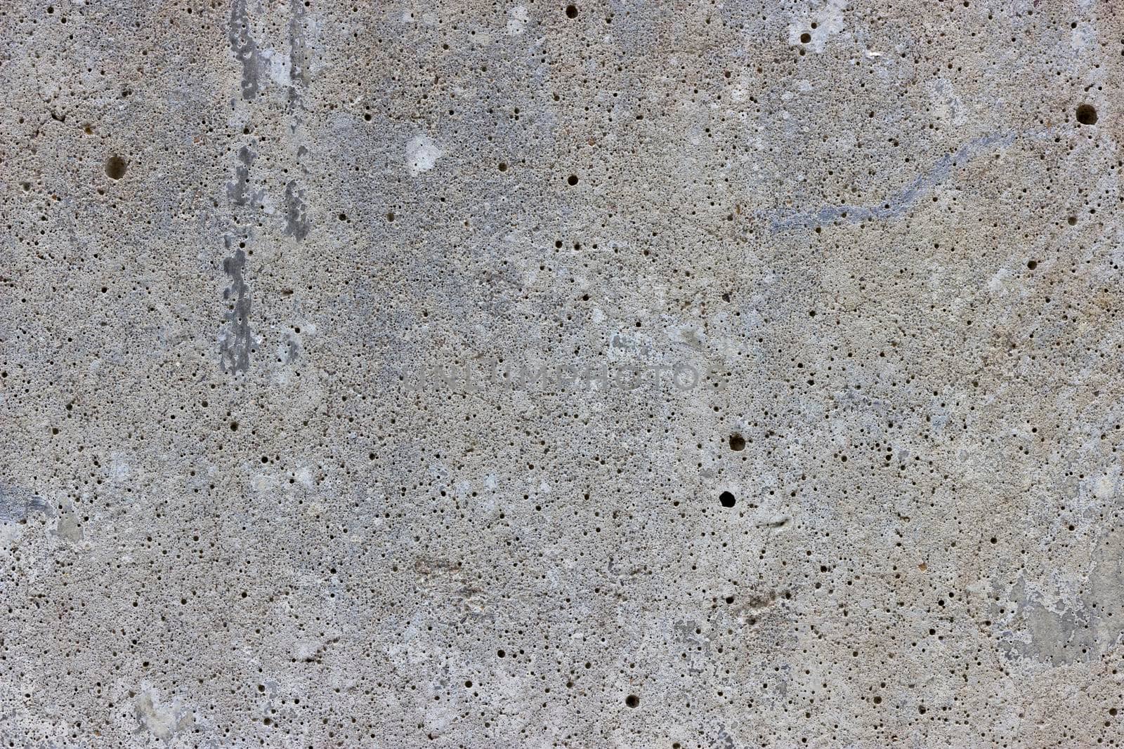 A flat grey concrete surface. The surface is textured and covered in holes from lots of tiny air bubbles.