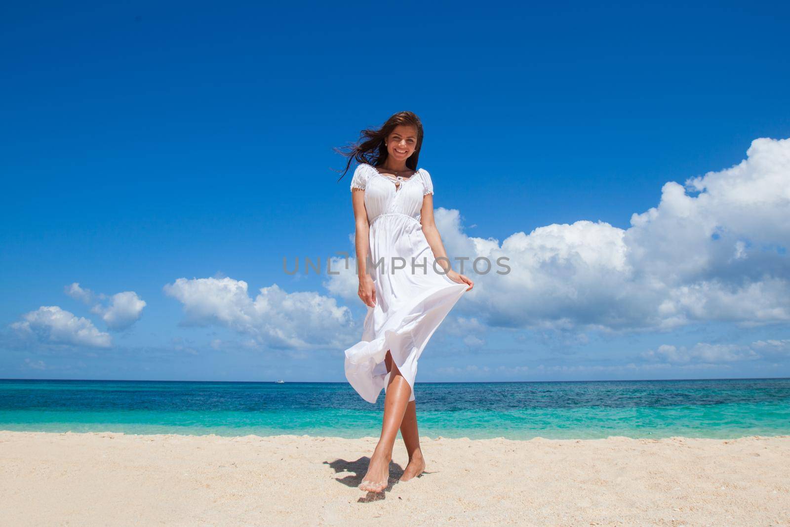 Woman in white dress walking on tropical beach, tropical sea on background