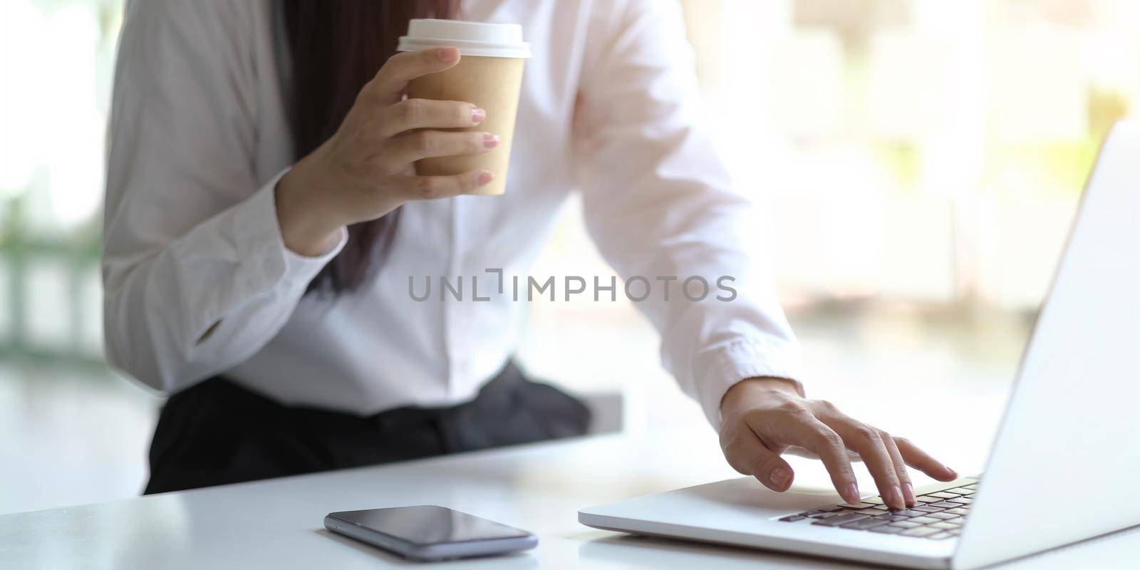 hands of a women holding a cup of coffee and typing on a laptop, office work concept. work online concept..