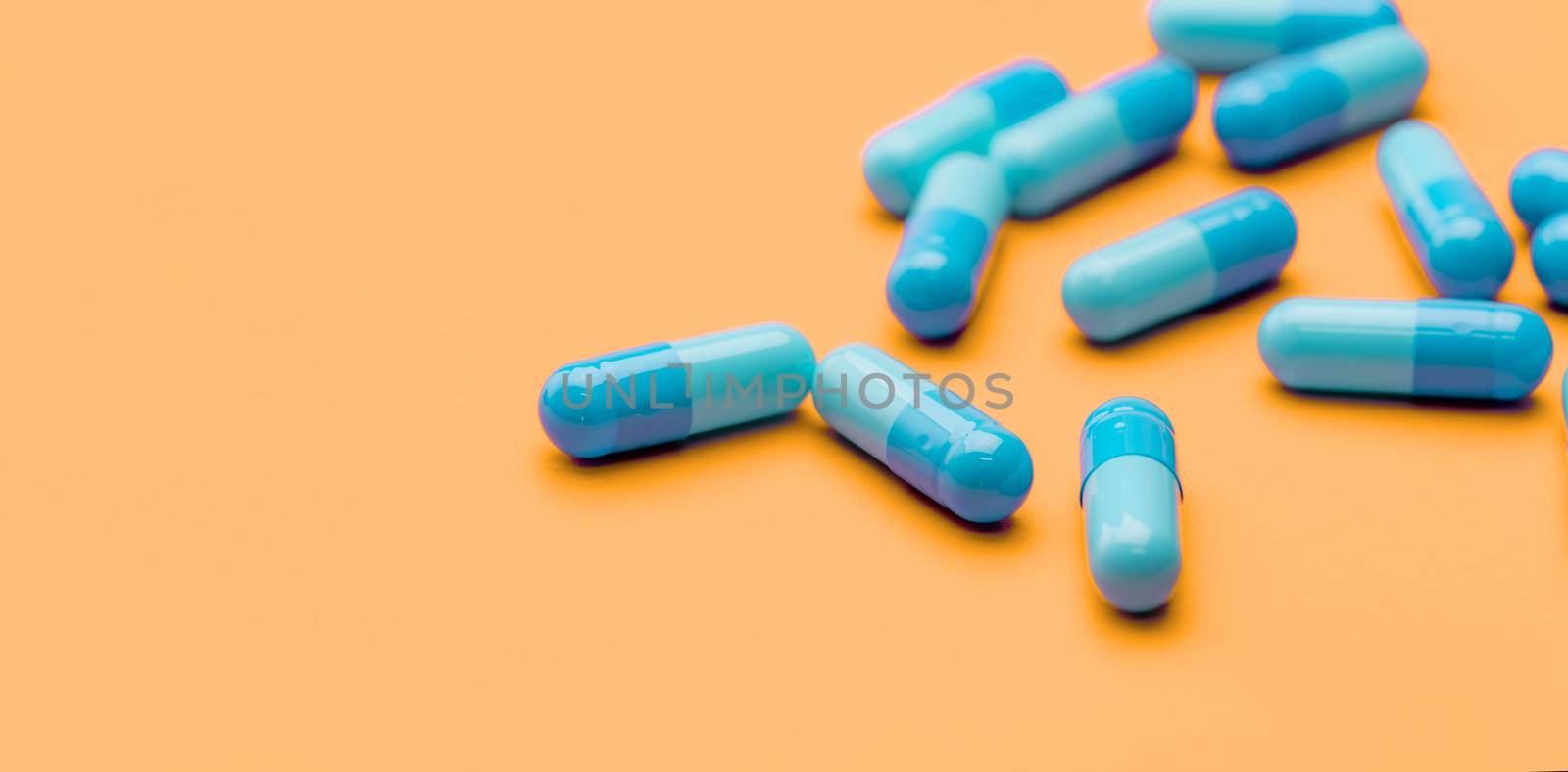 Blue antibiotic capsule pills spread on yellow background. Antibiotic drug resistance. Pharmaceutical industry. Healthcare and medicine concept. Health budget concept. Capsule manufacturing industry.