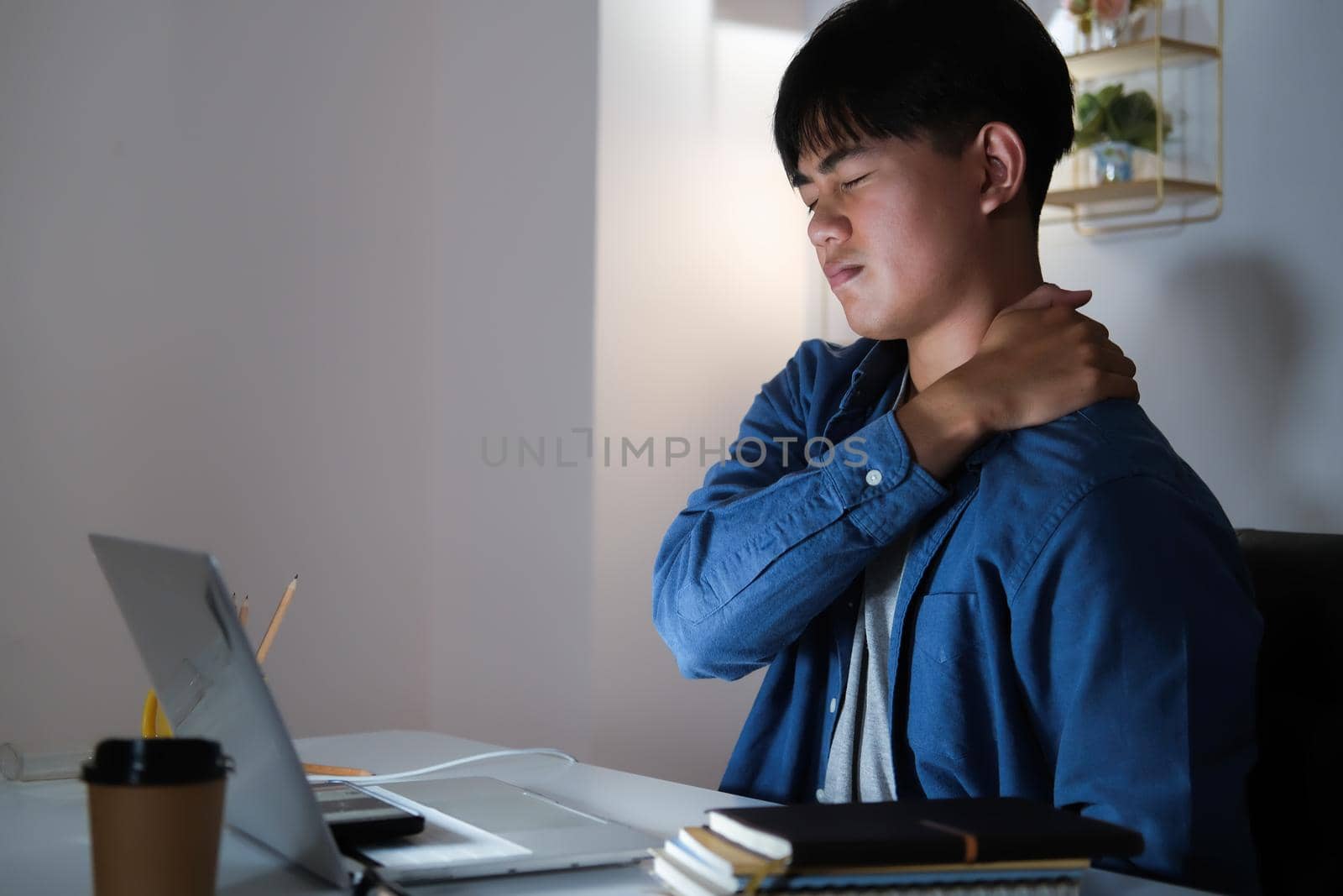 Young man overtime work and feel shoulder and neck pain at home.
