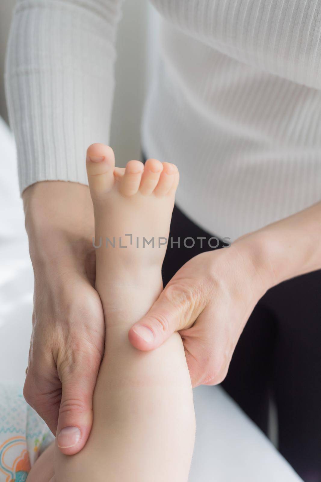 Mom gives her baby a leg and foot massage. Close-up. A satisfied baby lies on the massage table.