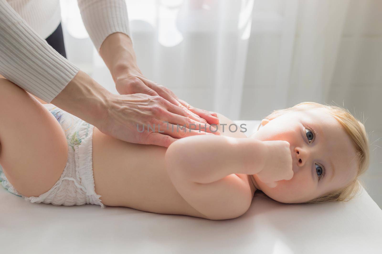 Mom gives her baby a tummy massage. Close-up. A satisfied baby lies on the massage table.