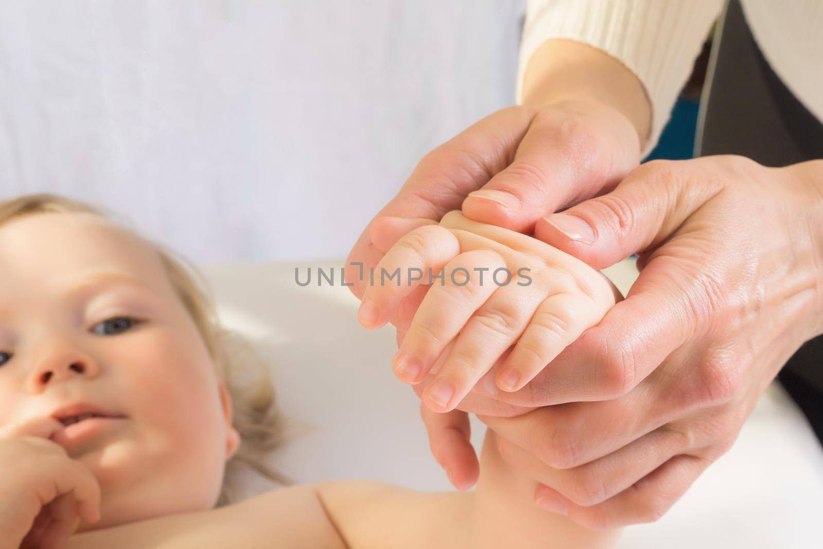 Mom gives her baby a hand massage. Close-up. A satisfied baby lies on the massage table.