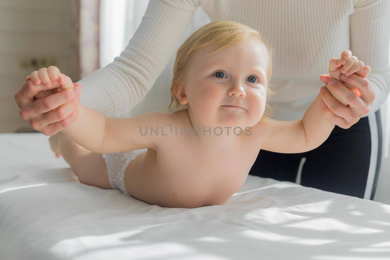 Mom does hand exercises to the baby. Close-up. A satisfied baby lies on the massage table on his stomach.