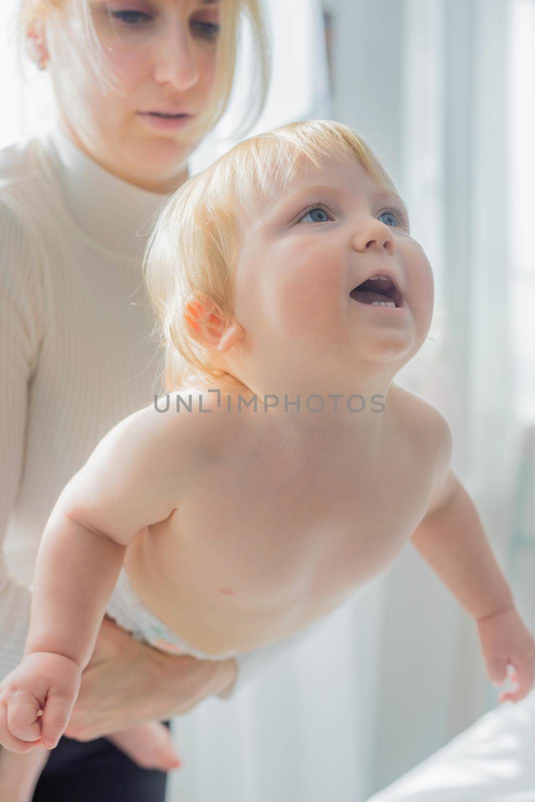 Mom does children's gymnastics for the baby, holding him by the chest. Close-up. Happy child is trying to climb.
