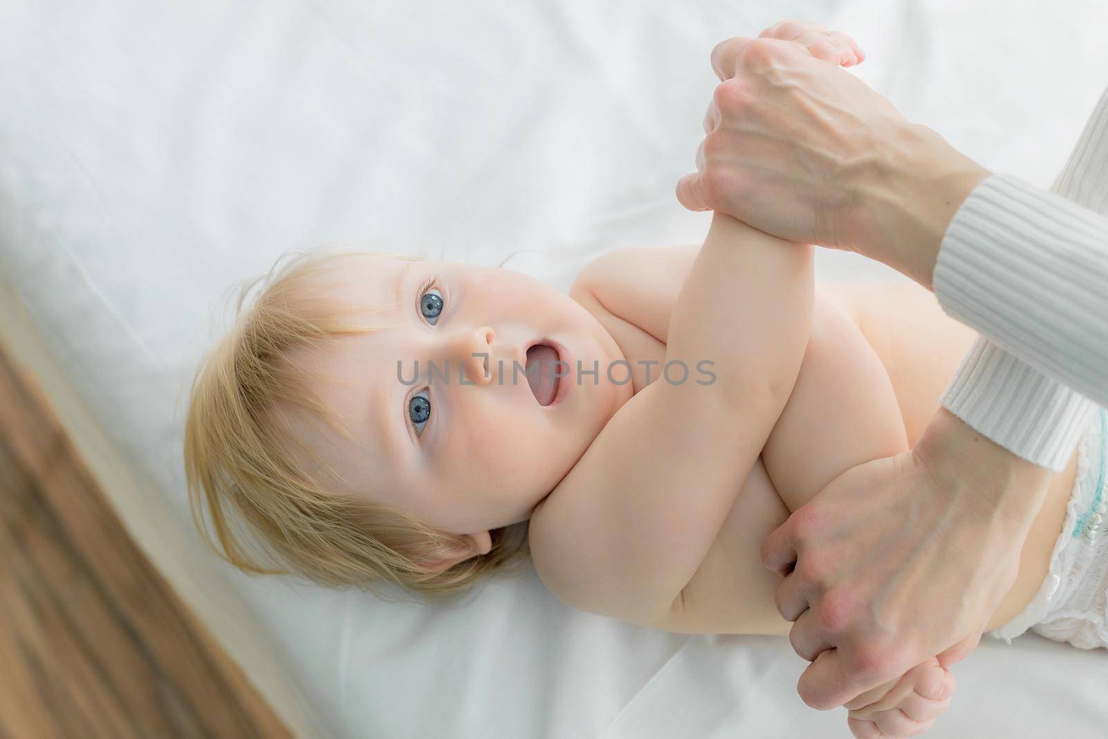 Mom does baby gymnastics for the baby's arms. Close-up. A happy child lies on his back.