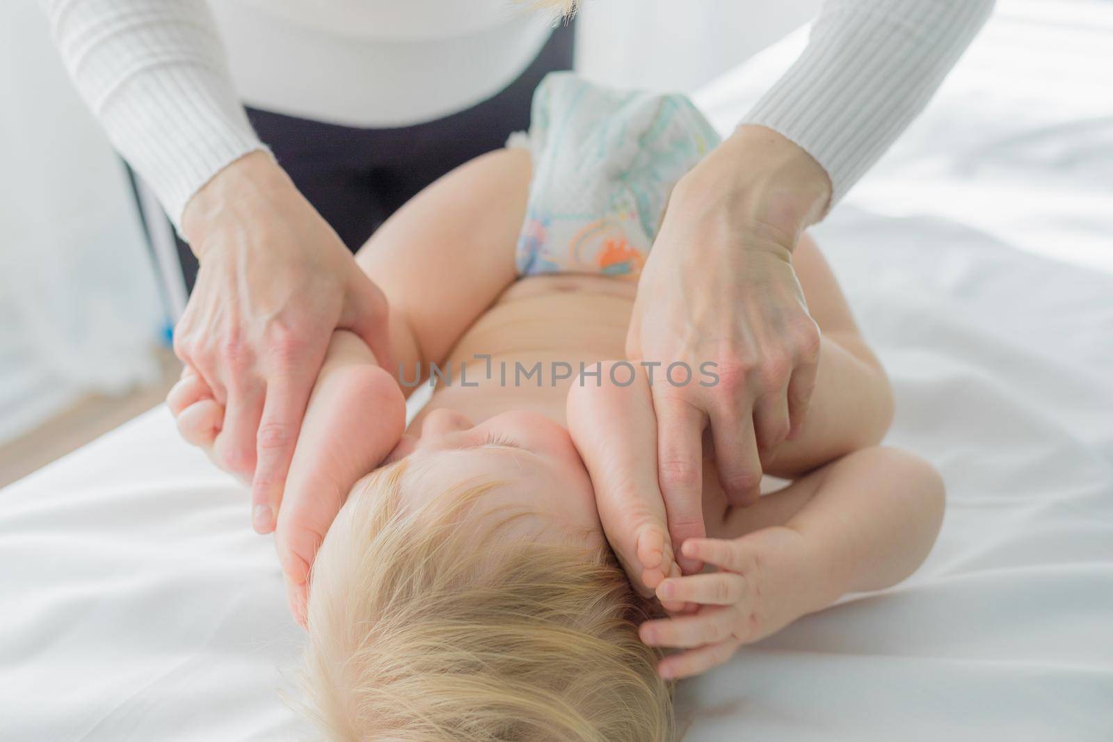 Mom does baby gymnastics for the baby's legs. Close-up. A happy child lies on his back.
