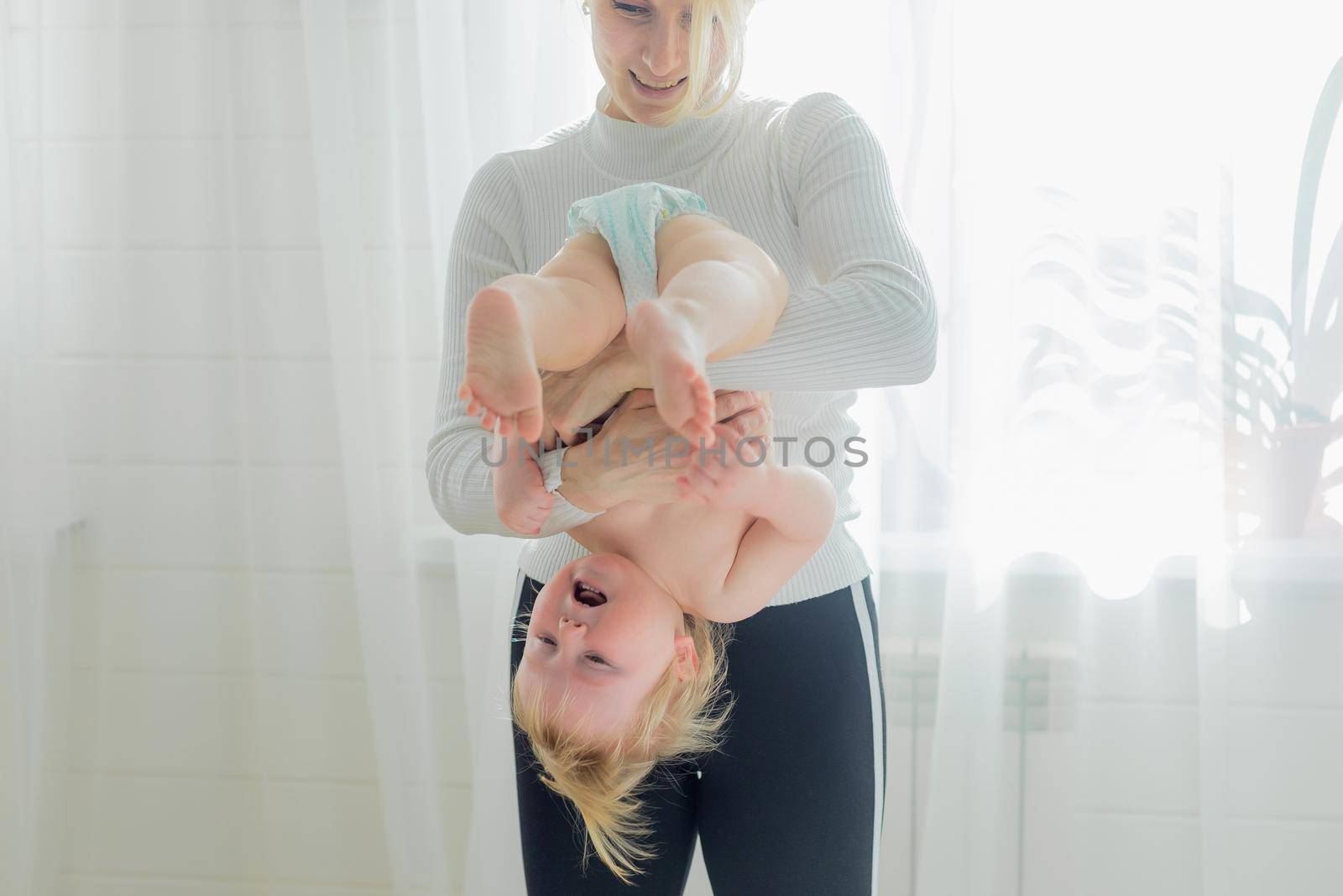 Mom holds the baby upside down, is engaged in children's gymnastics. by Yurich32