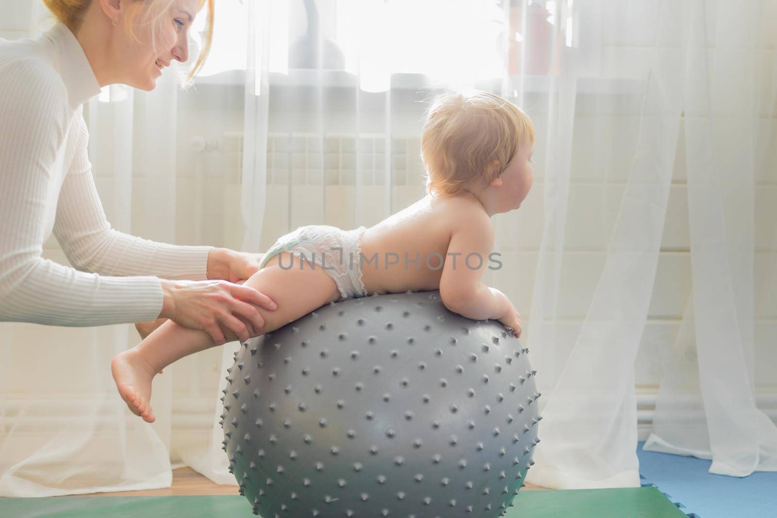 Mom is engaged in gymnastics with the baby on an inflatable ball. Fitball, gymnastics for a child.